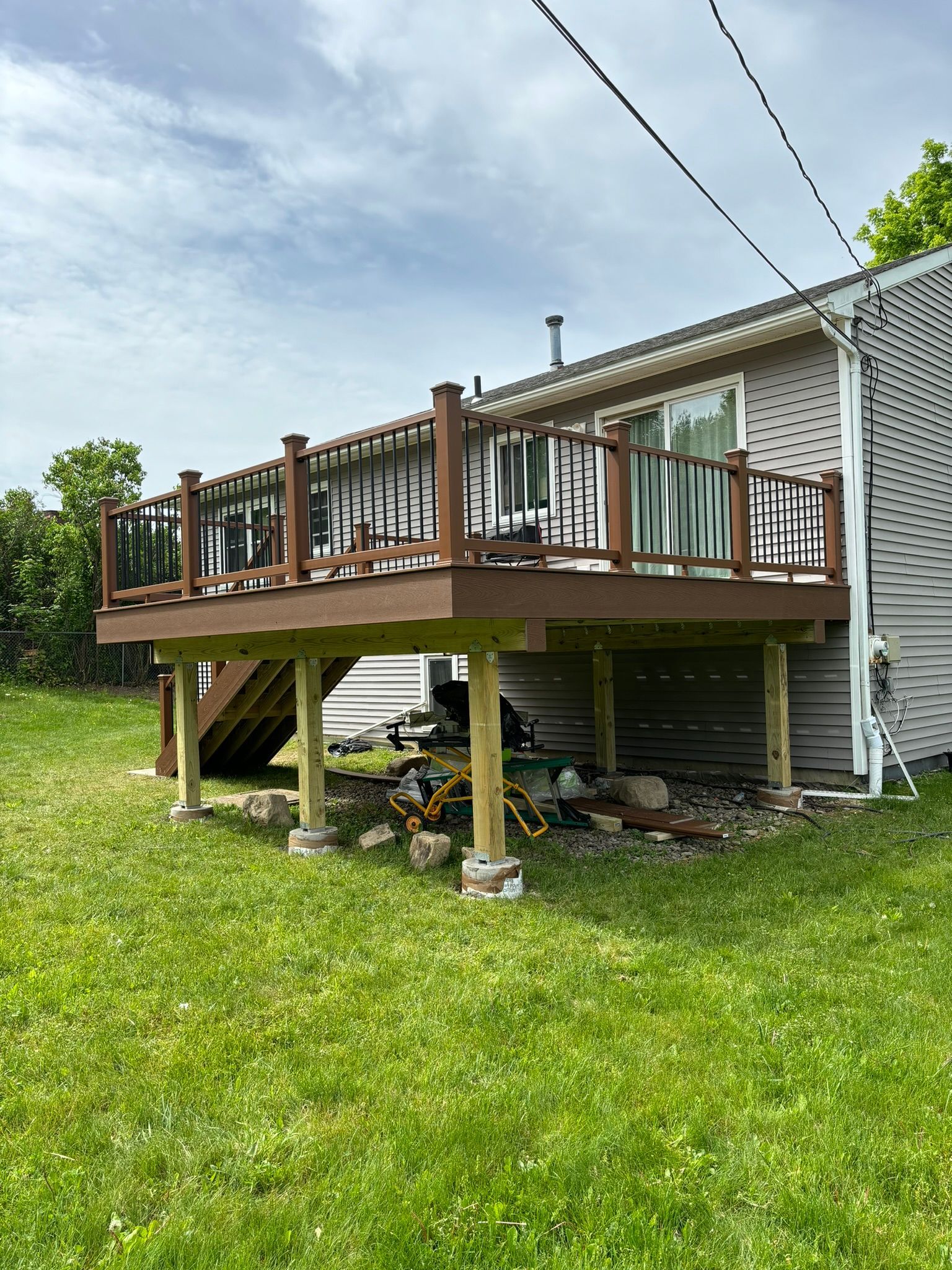 Wooden deck attached to a house with a green grassy yard and blue sky.
