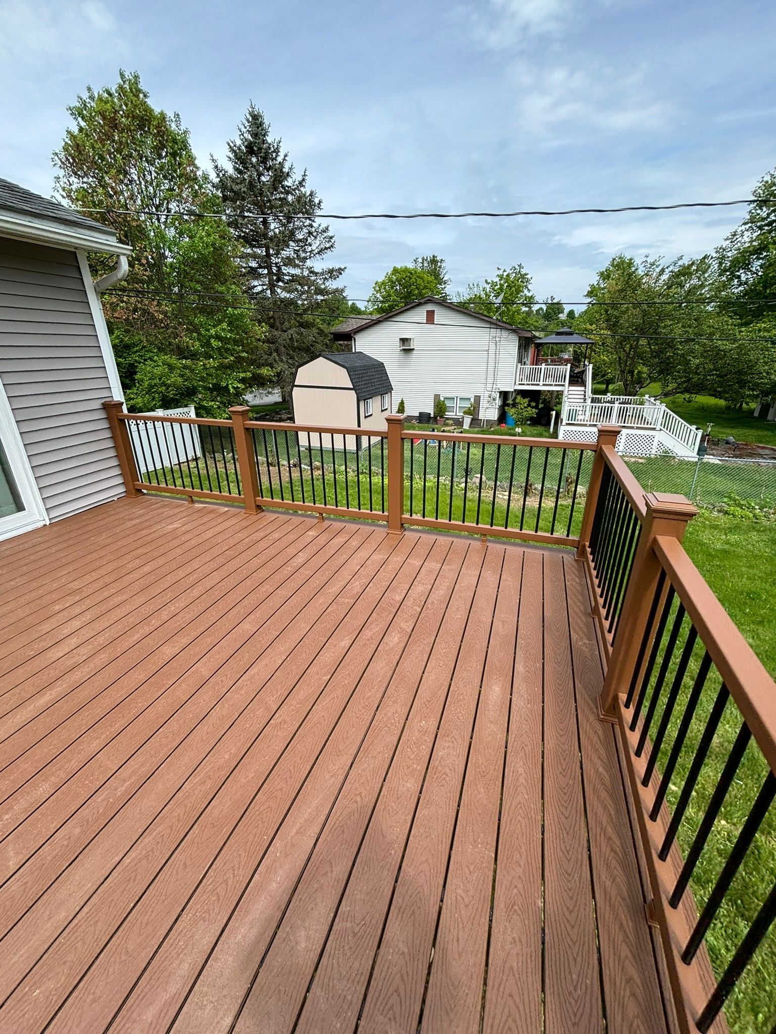 Wooden deck with brown planks, black railings, and a view of a backyard and houses on a cloudy day.