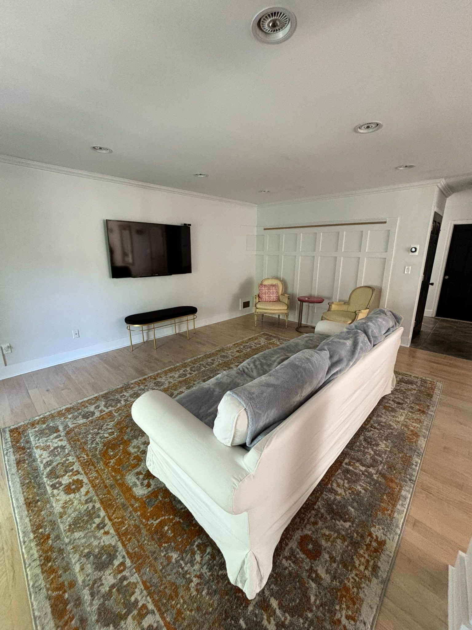 Living room with white sofa, TV, and patterned rug. Two small chairs and a table.