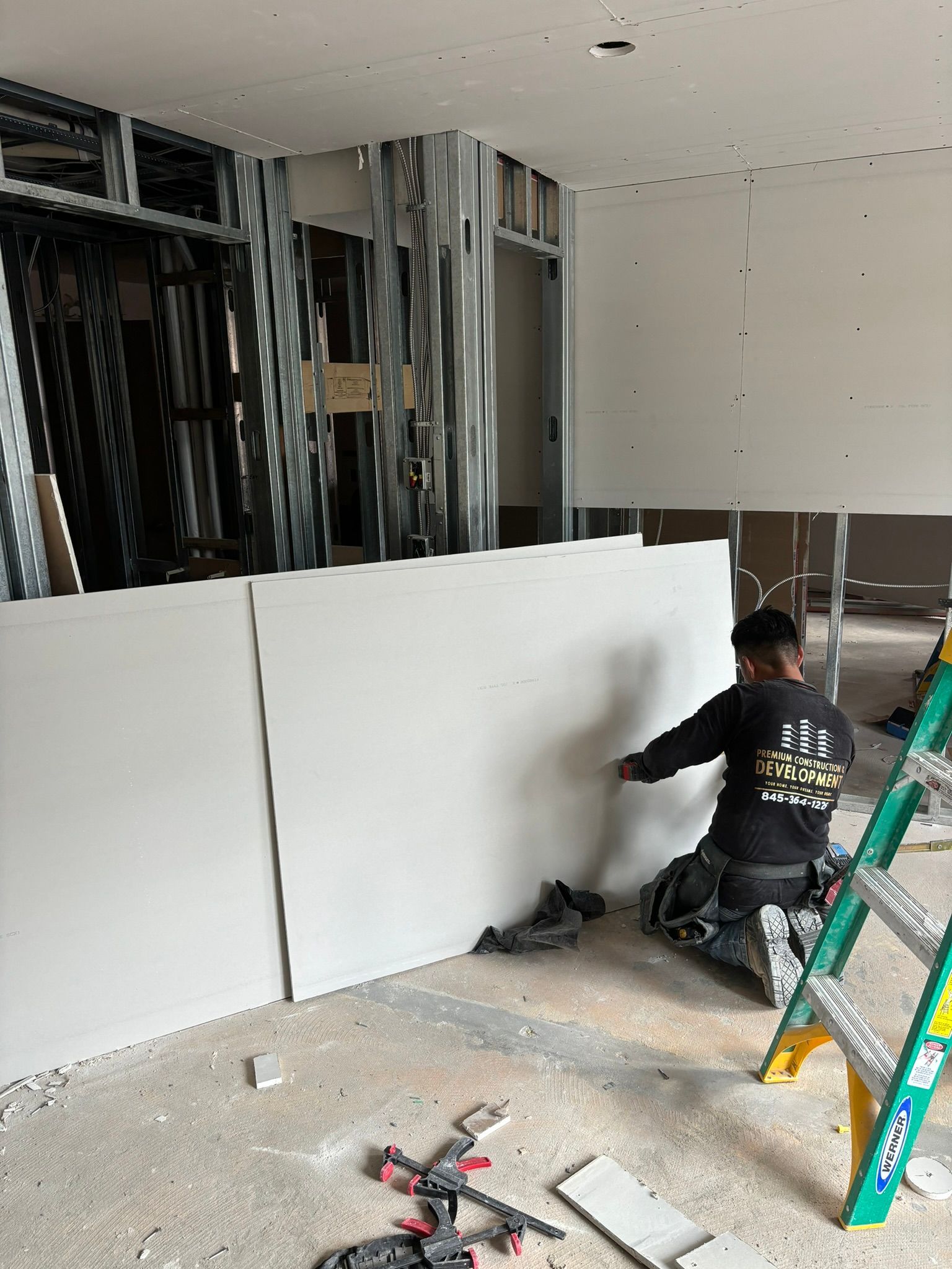 Construction worker installs drywall in a room with metal framing.