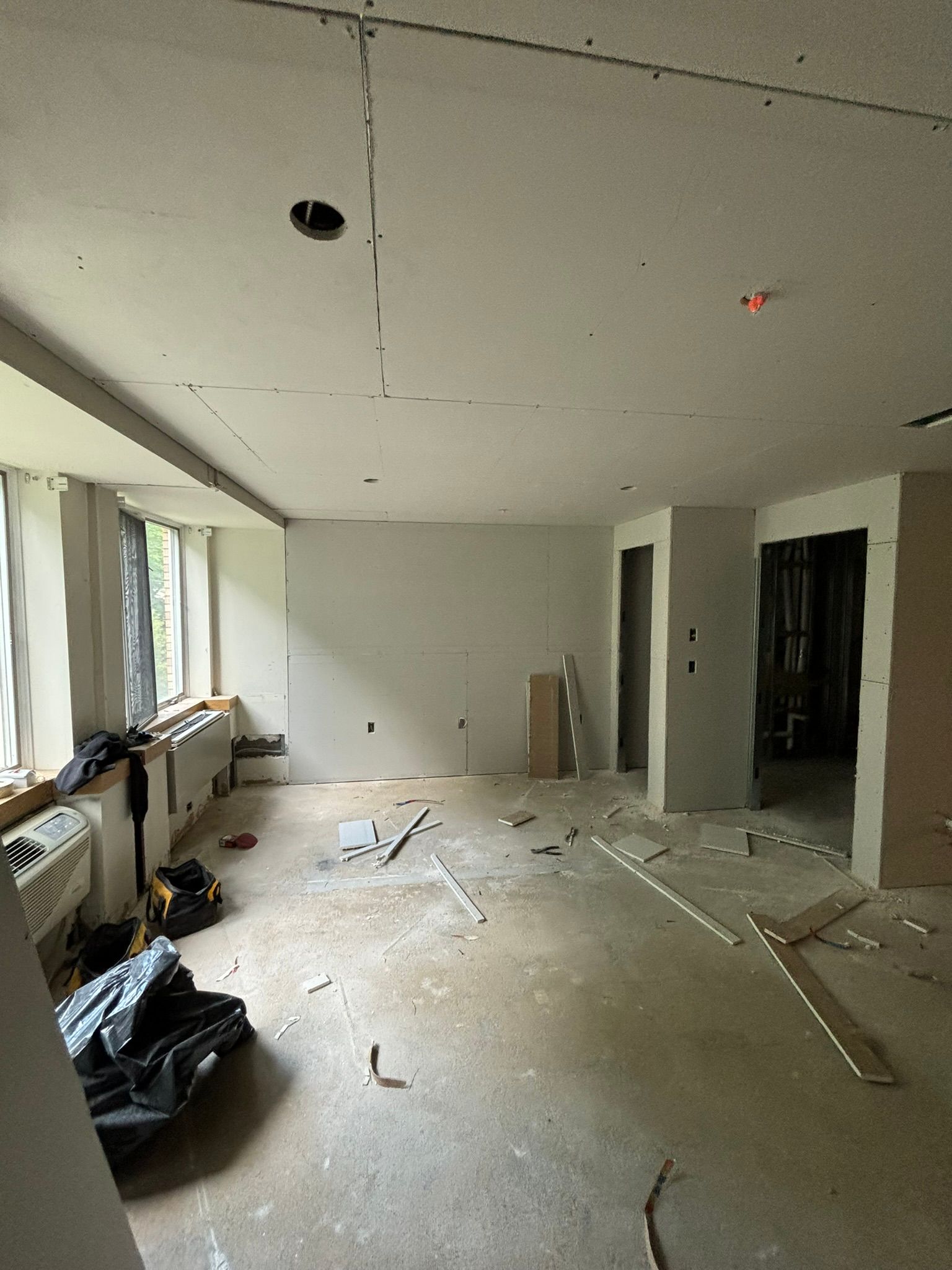 Interior room under construction, drywall on walls and ceiling, tools on floor.