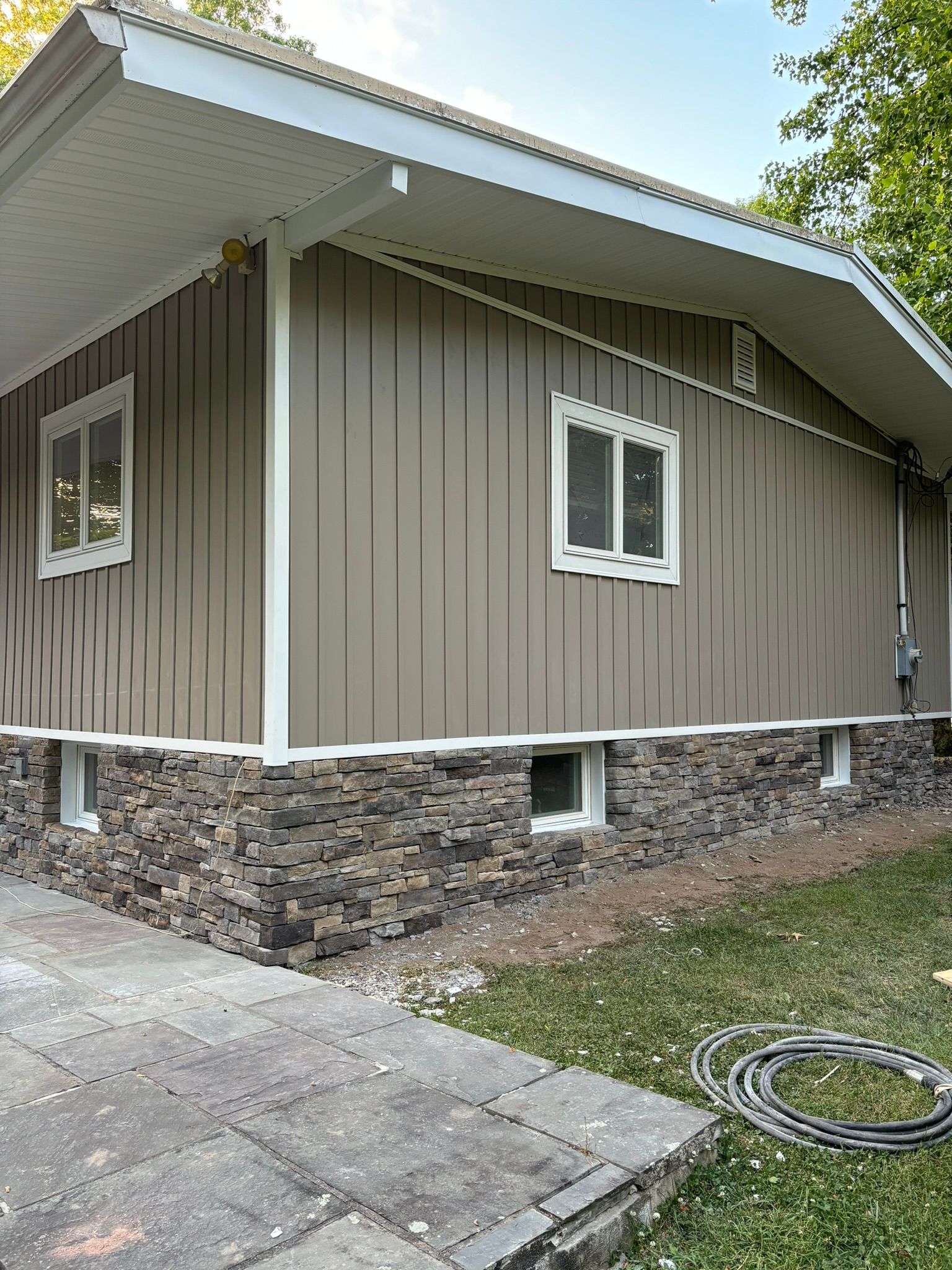Tan siding house with stone base, white trim, and windows.