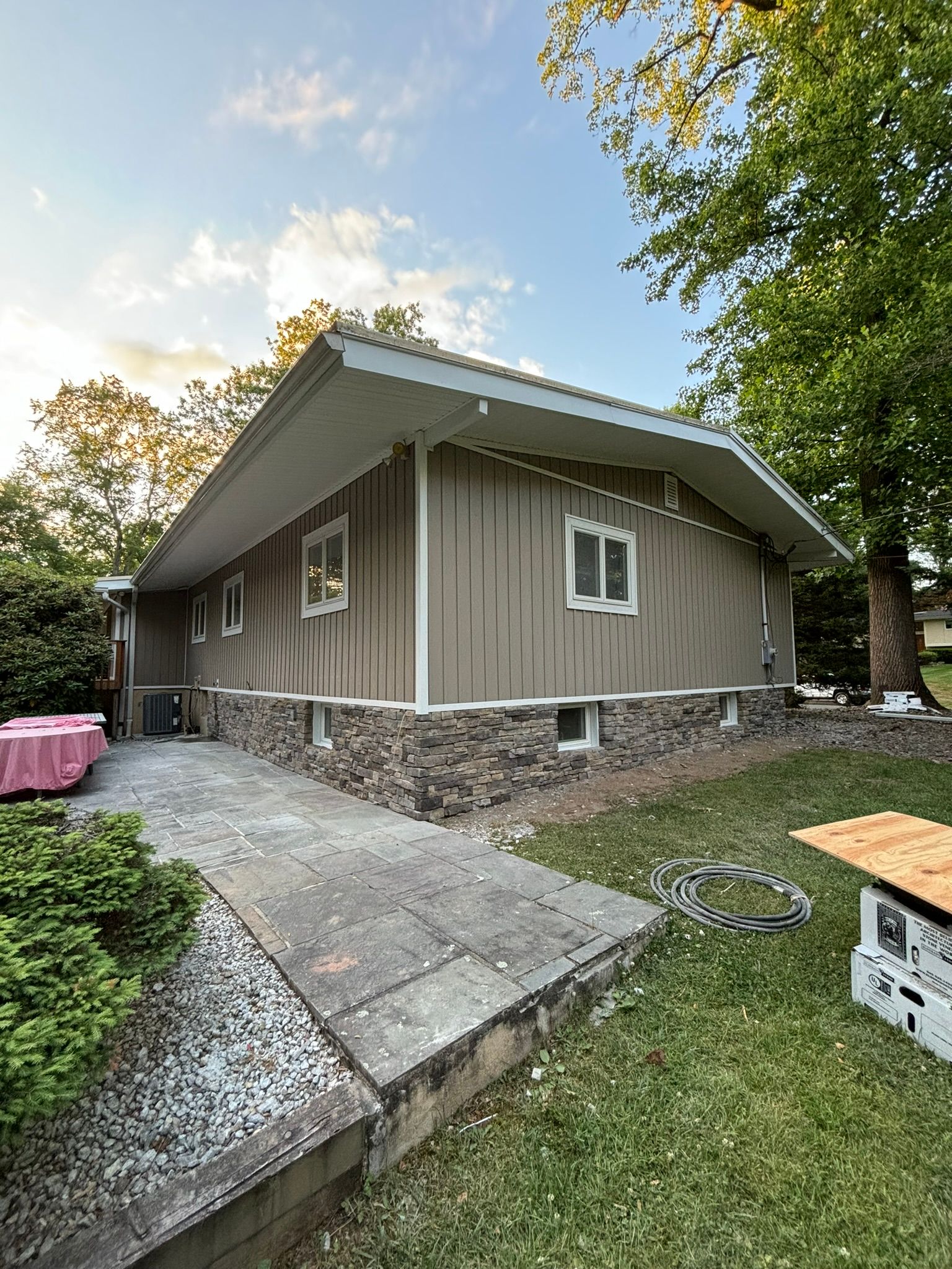 Tan house with stone foundation, two windows, and a concrete patio.