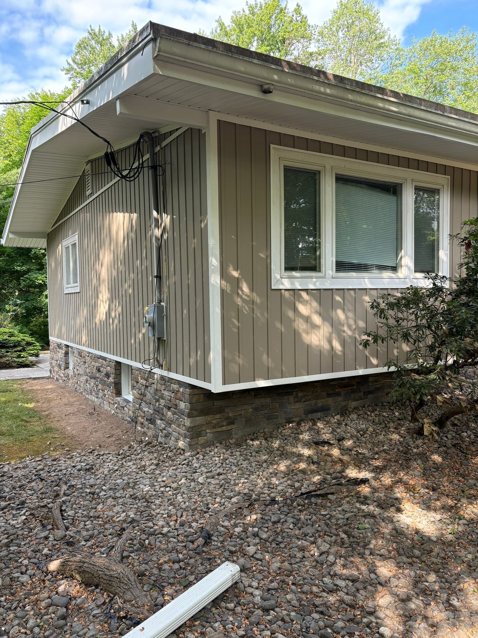 Tan house with white trim, a stone foundation, and a gravel-covered slope.