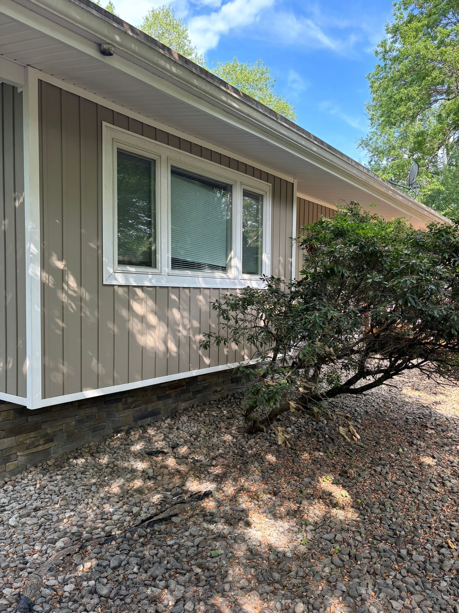 Tan house exterior with white trim, window, and shrubbery in a gravel bed.