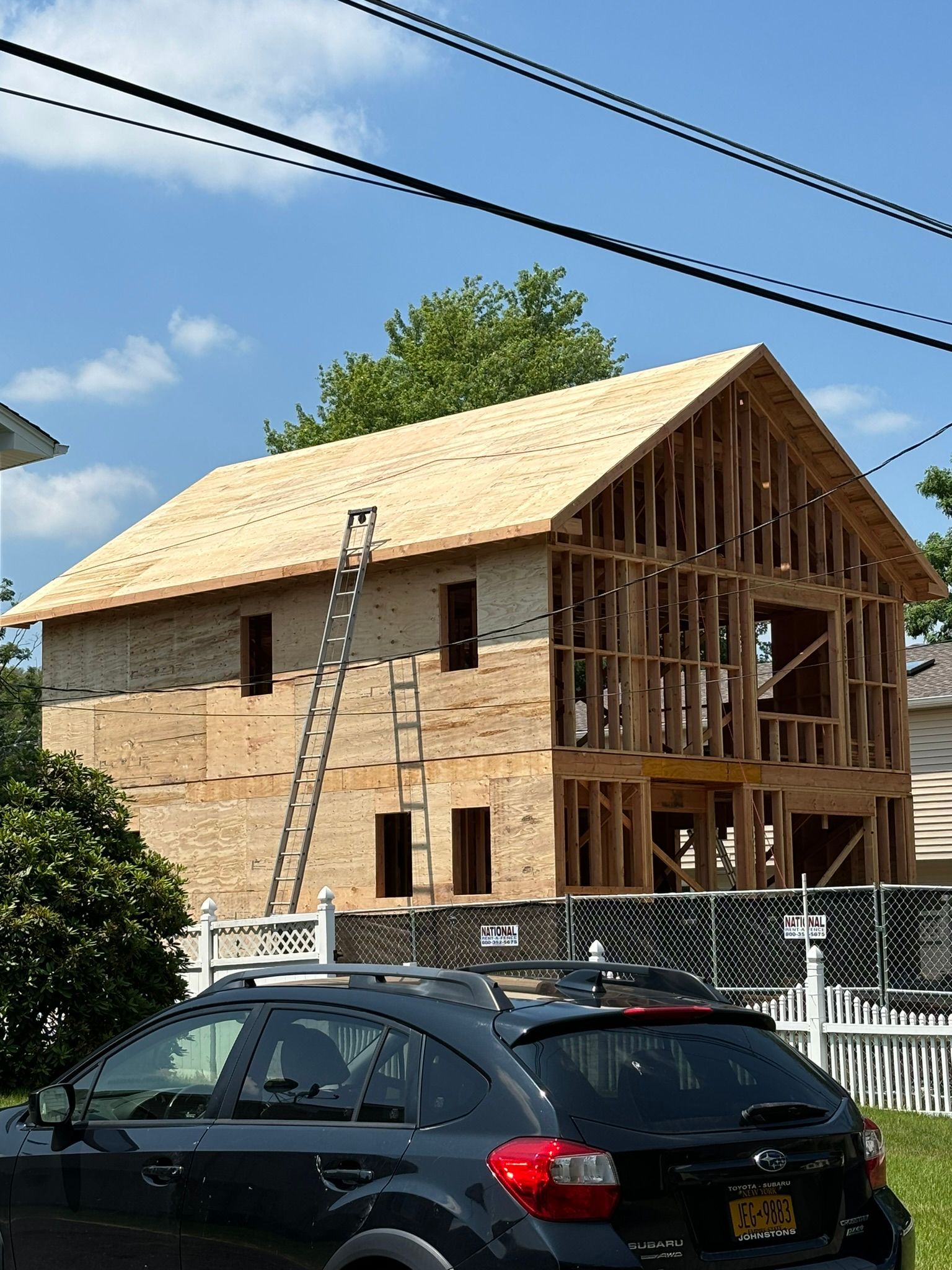 House under construction with wooden frame and plywood, ladder, blue sky.