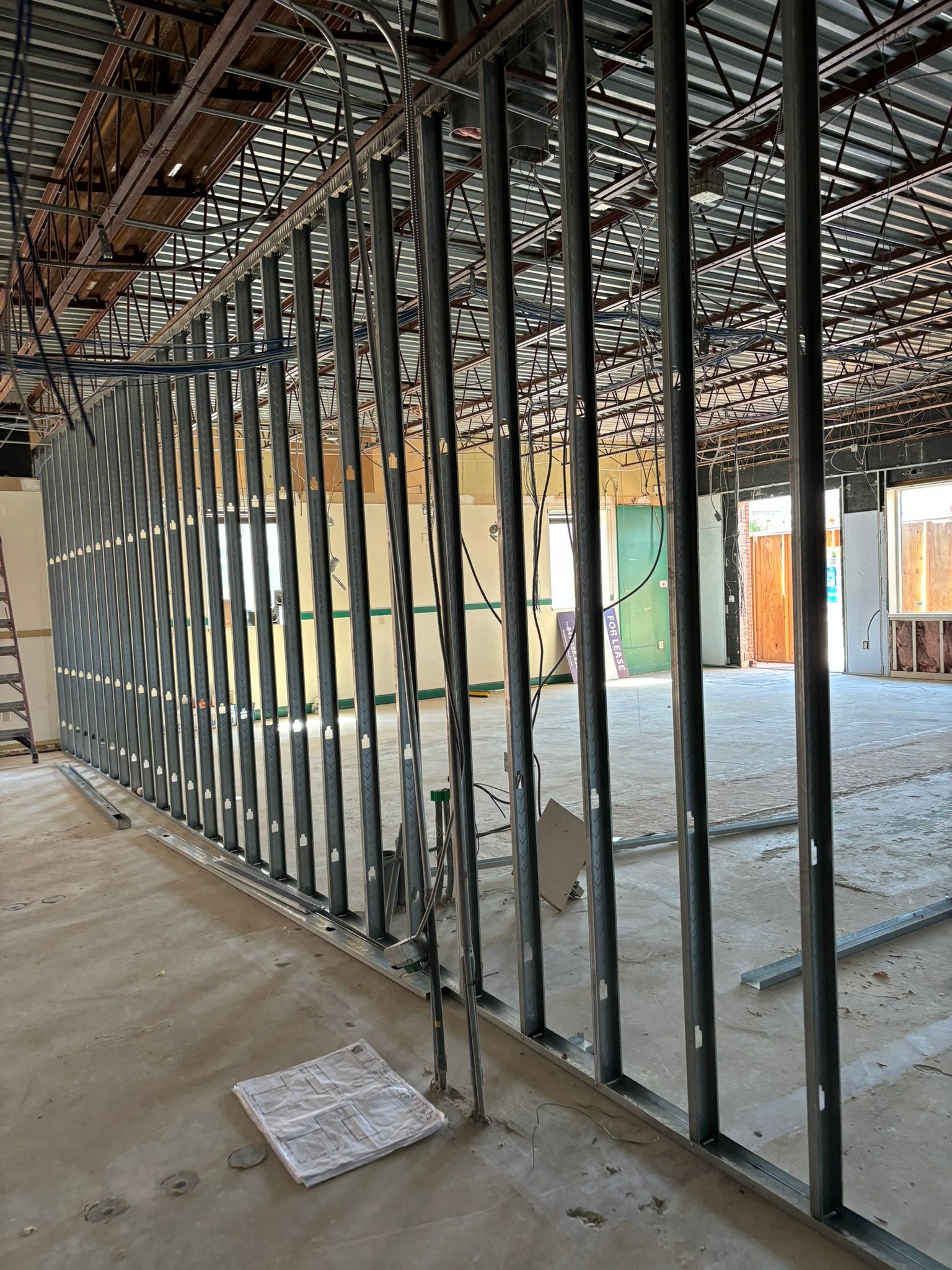 Interior construction site with metal studs forming a wall, ceiling beams, and concrete floor.
