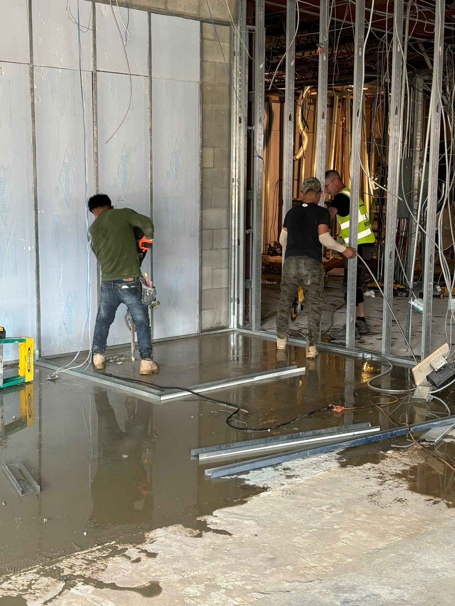 Construction workers installing wall panels and framing. Water on the floor.