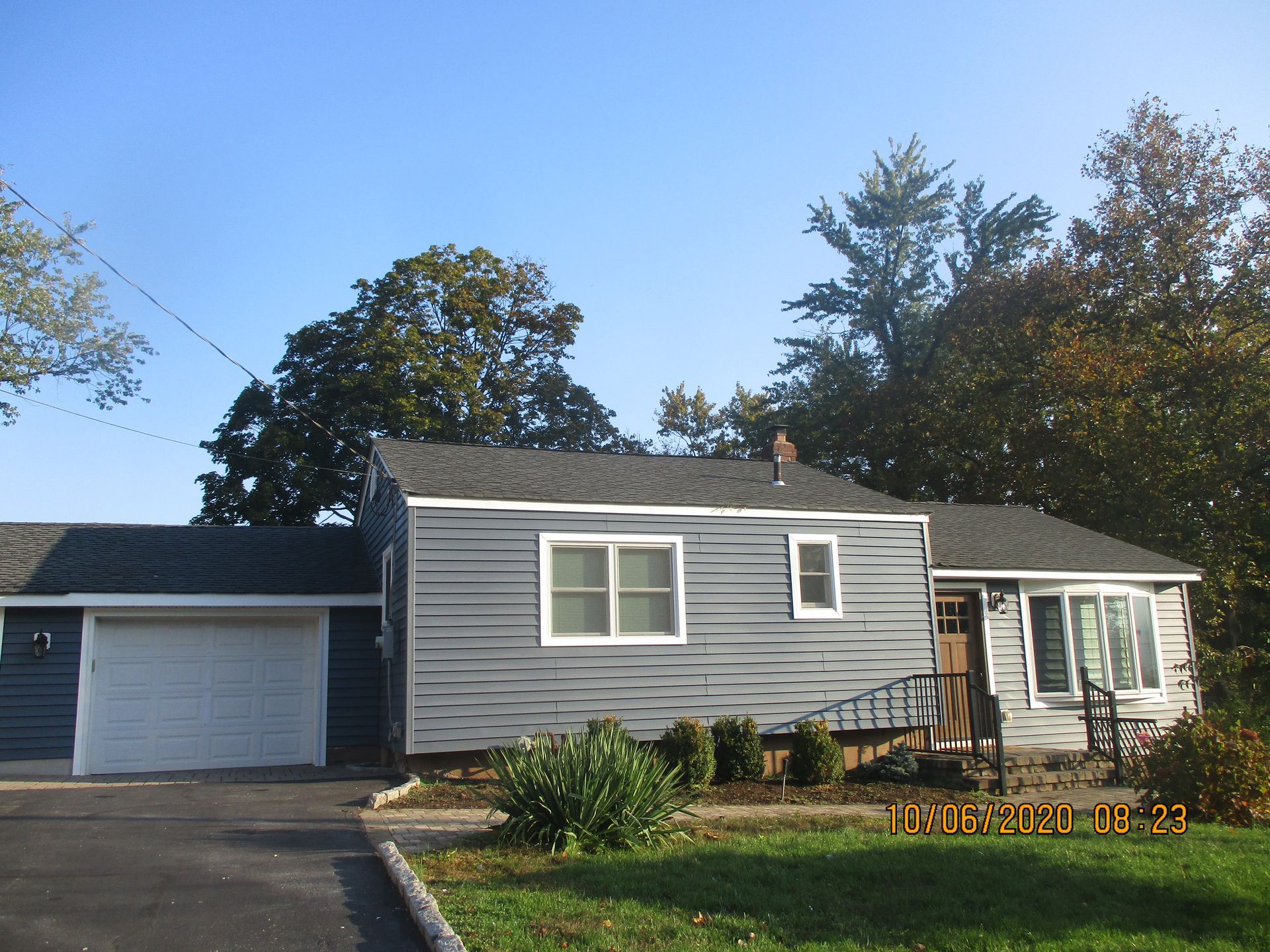 Blue house with attached garage, small bushes, and driveway.