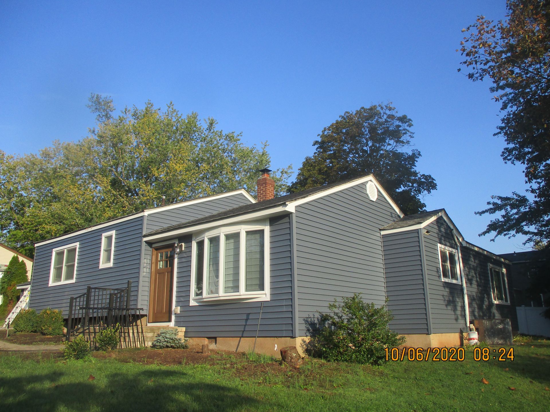 Blue-sided house with white trim, bay window, and brown door under a clear sky.