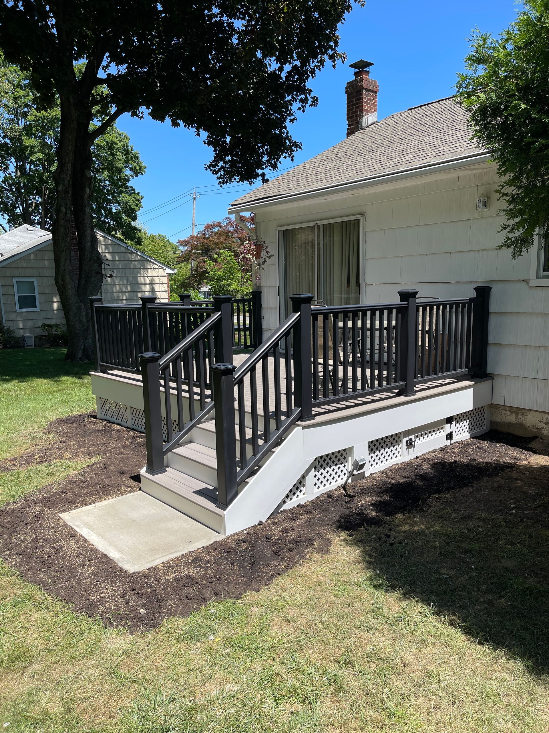 Black deck with steps and railing attached to a white house. Mulch and grass surround.