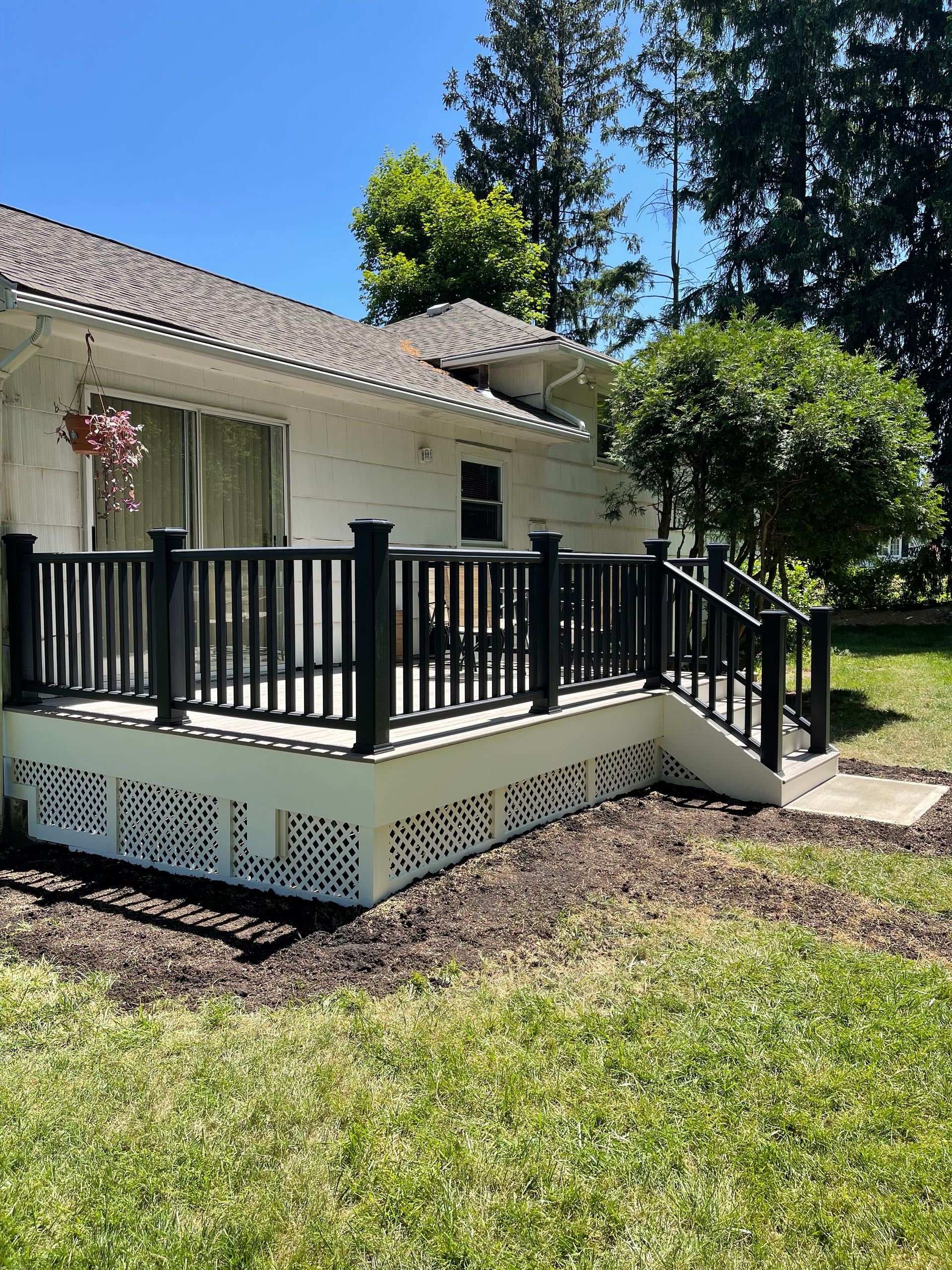 Black-railed deck attached to a white house. Gravel and grass surround it.