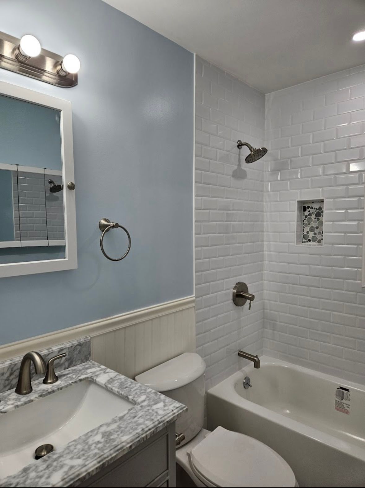 Blue and white bathroom with marble vanity, subway tile shower, and a silver-colored faucet.