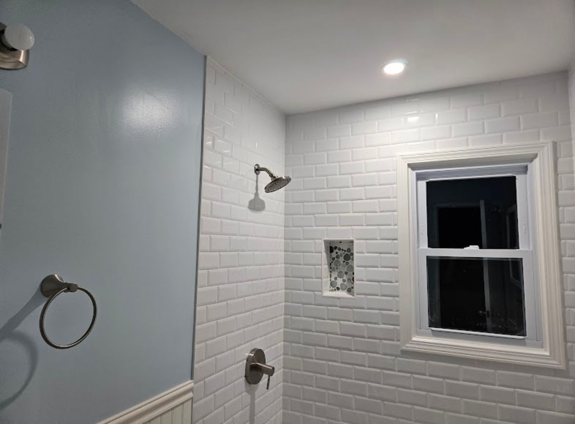Bathroom with white subway tile shower, light blue wall, and a window.