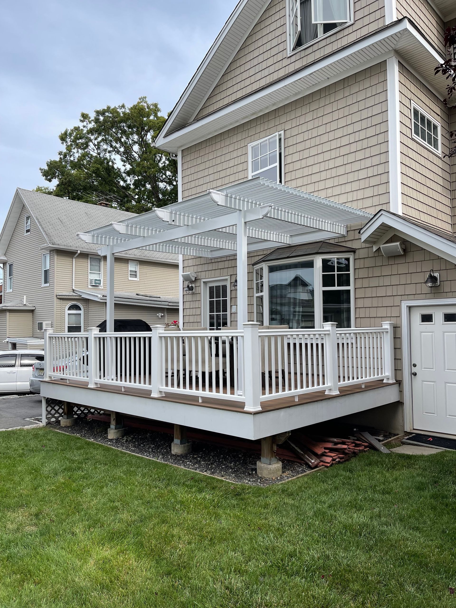 White deck with pergola attached to a tan house. Lawn in the foreground.