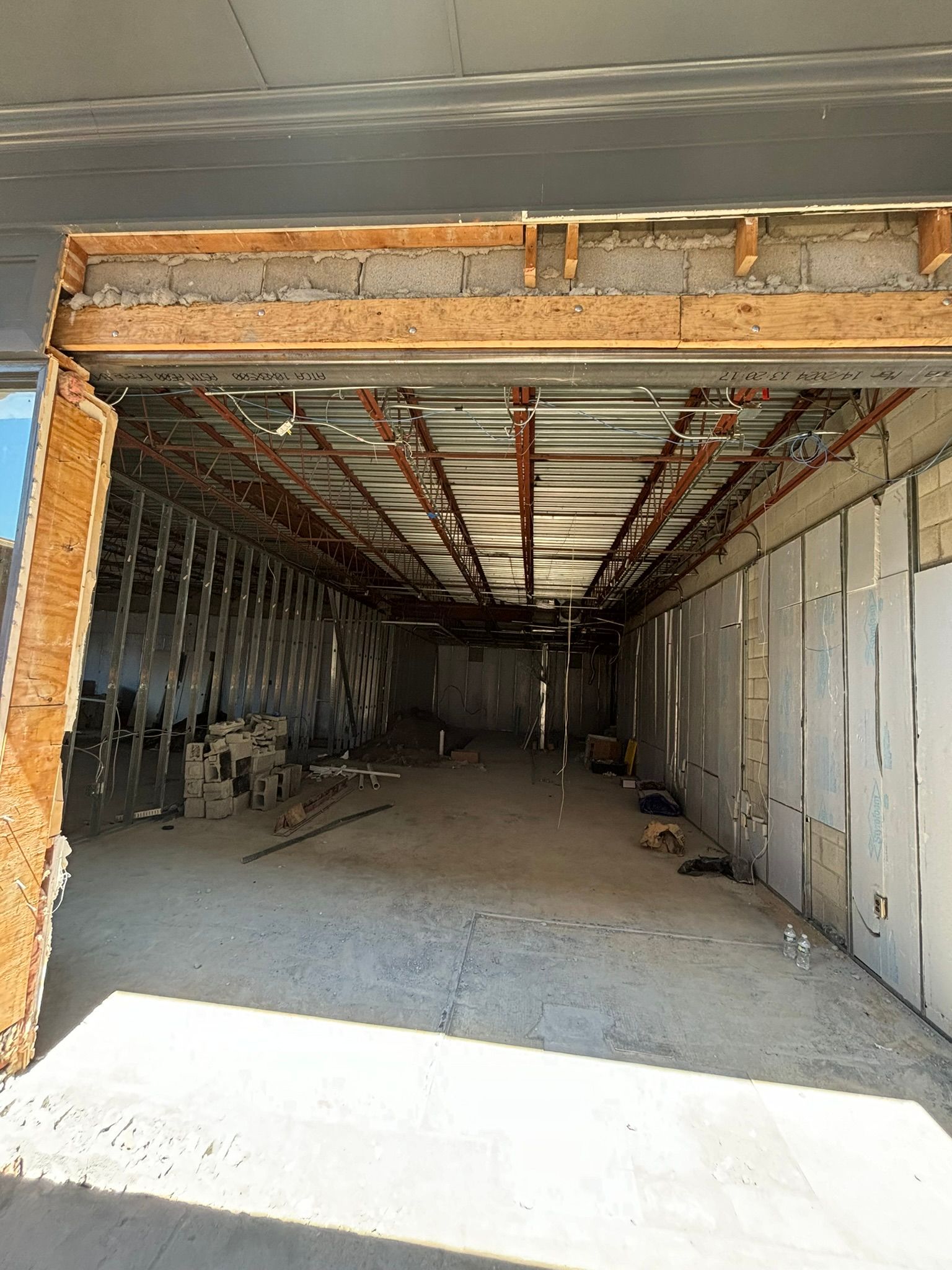 Construction of a long, narrow room. Walls are unfinished with exposed beams and drywall.