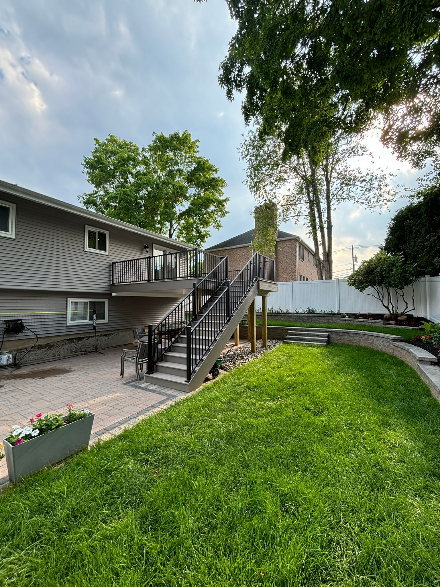 Backyard with deck, stairs, and green lawn leading to a house. Gray siding on the house and a white fence.