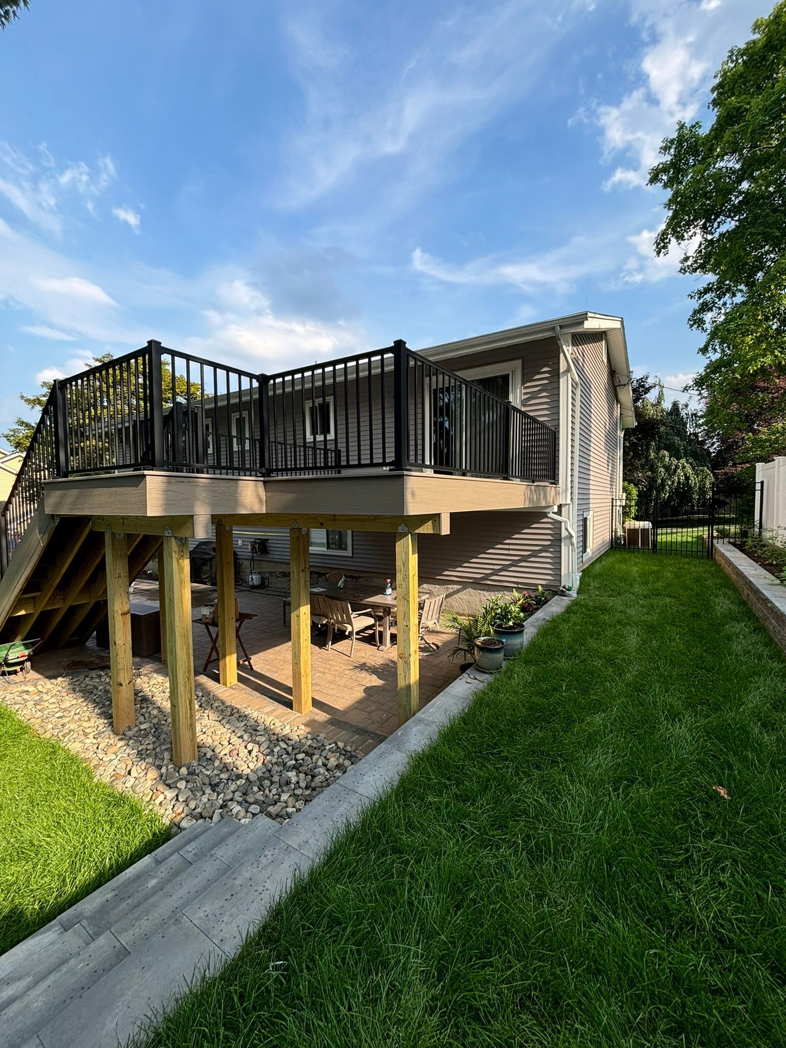 Elevated deck with black railing attached to a house; green lawn, blue sky.