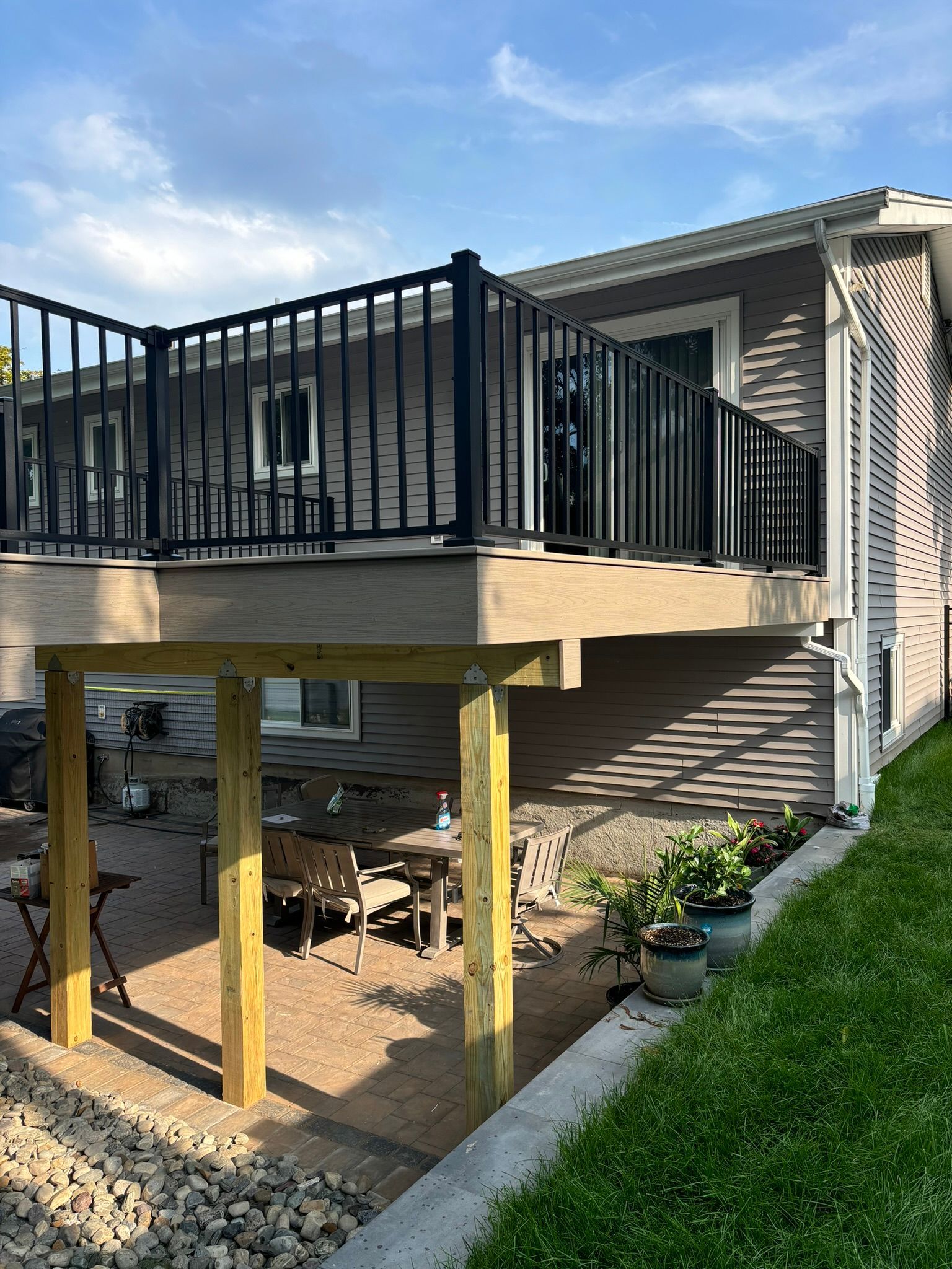 Raised deck with black railing, supported by wooden posts, overlooking a patio.