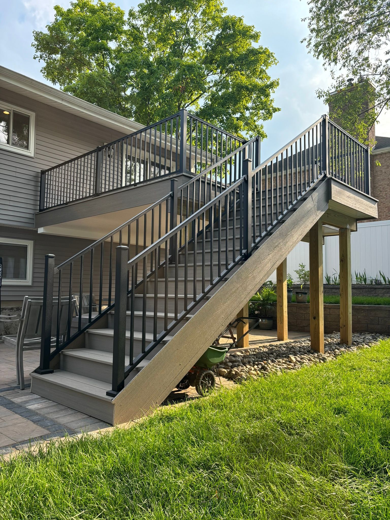 Two-story deck with black railings and gray steps. Green grass and trees in the background.