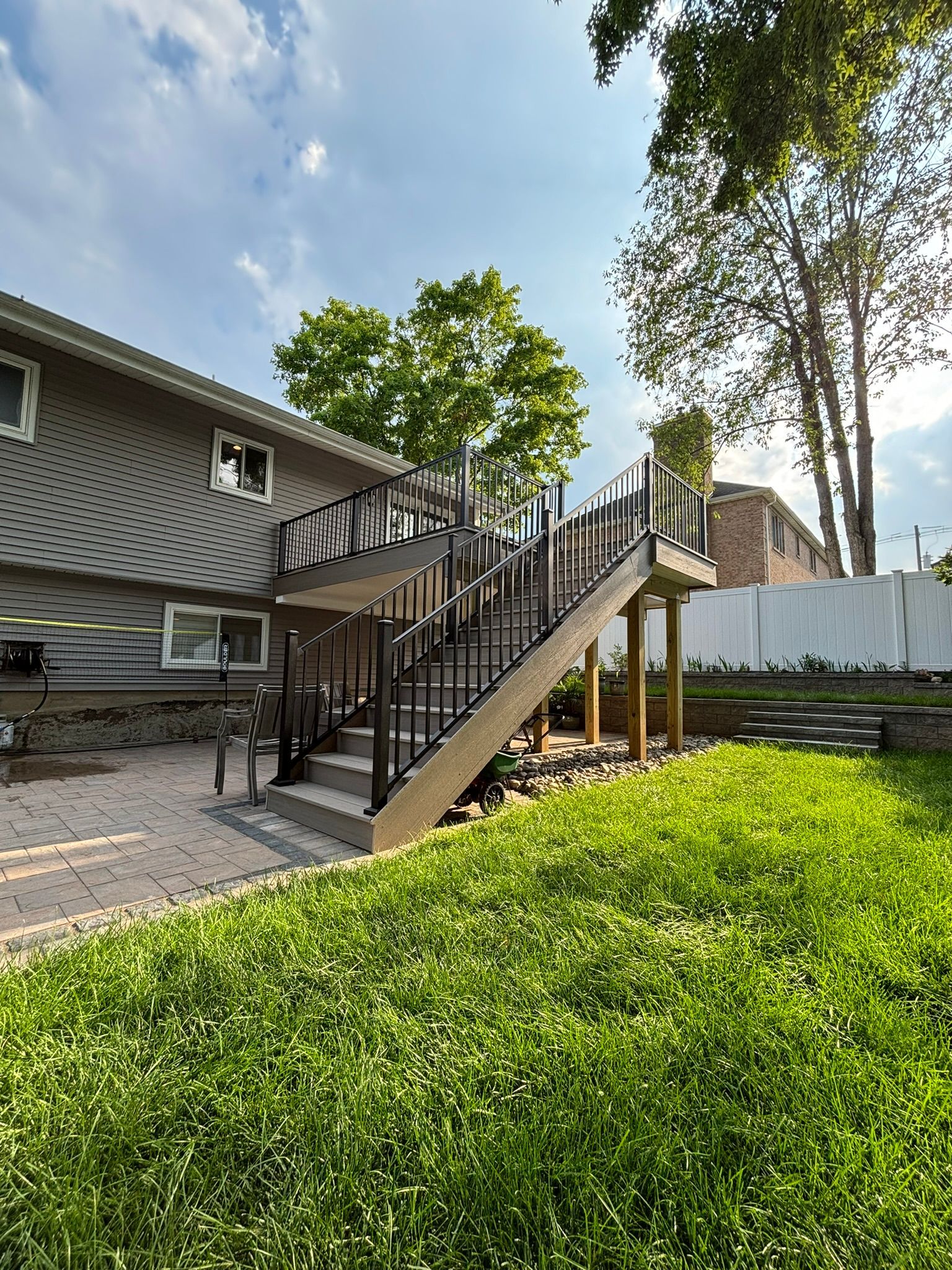 Backyard view of a two-story deck with black railings and stairs, attached to a gray house; green grass.