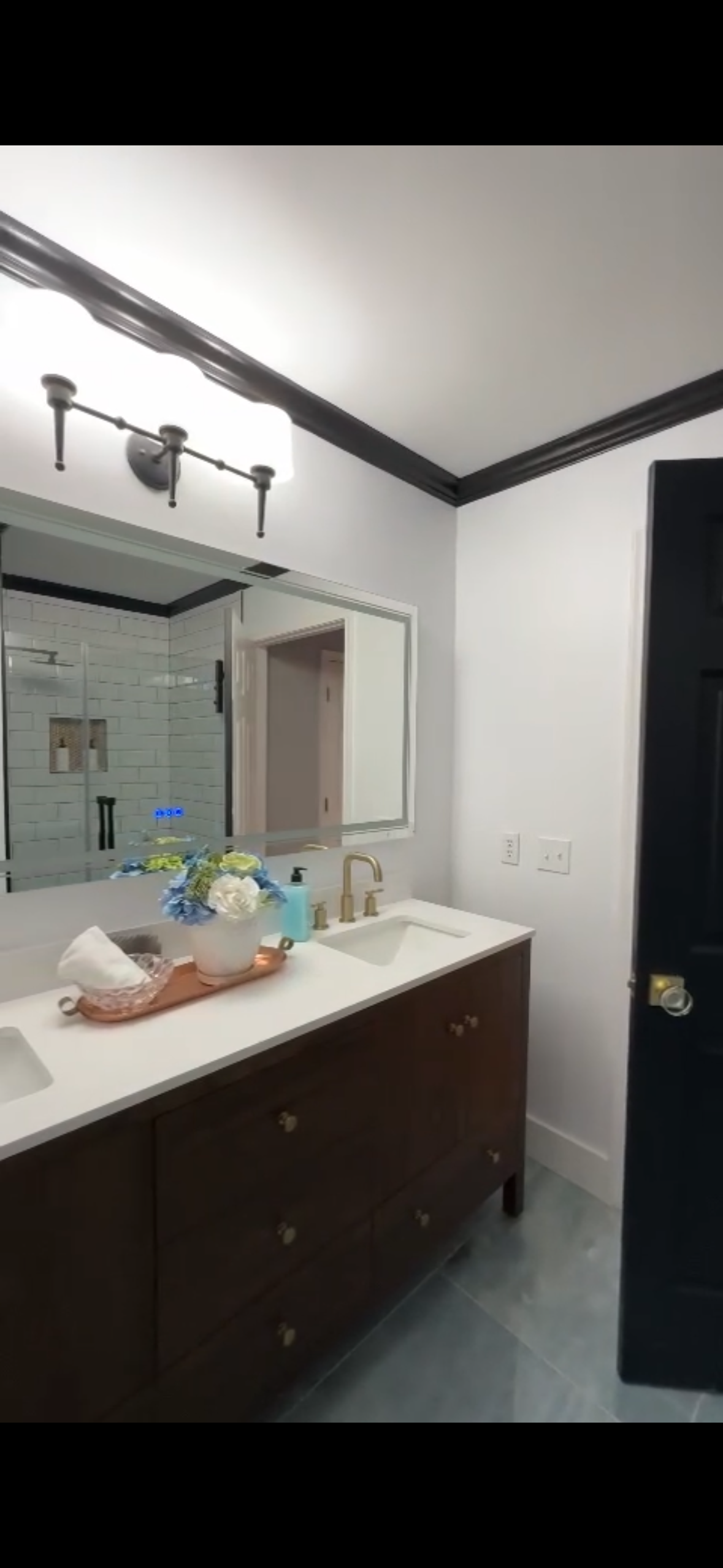Bathroom with white walls, dark trim, brown vanity, and black door.