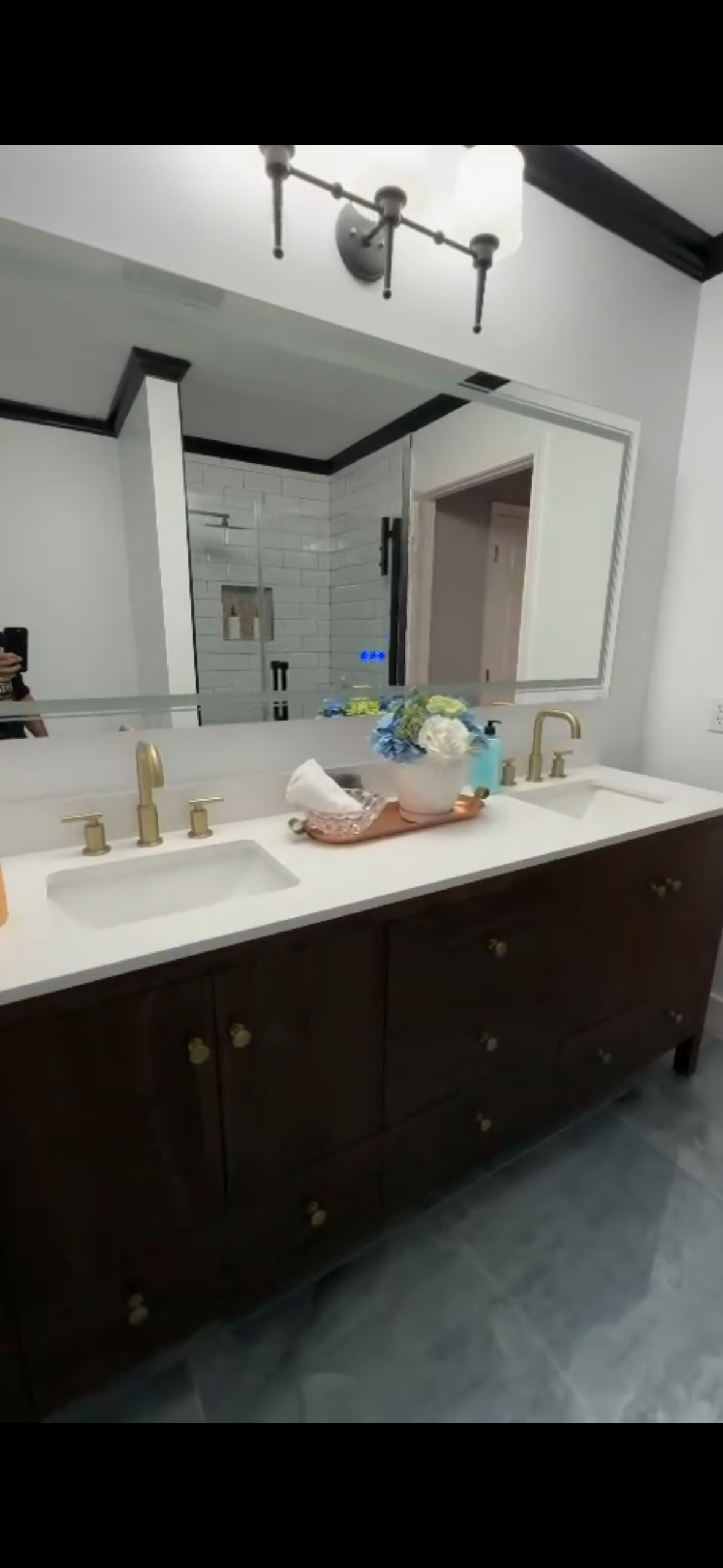 Bathroom with dark brown vanity, white countertop, large mirror, and gold fixtures.