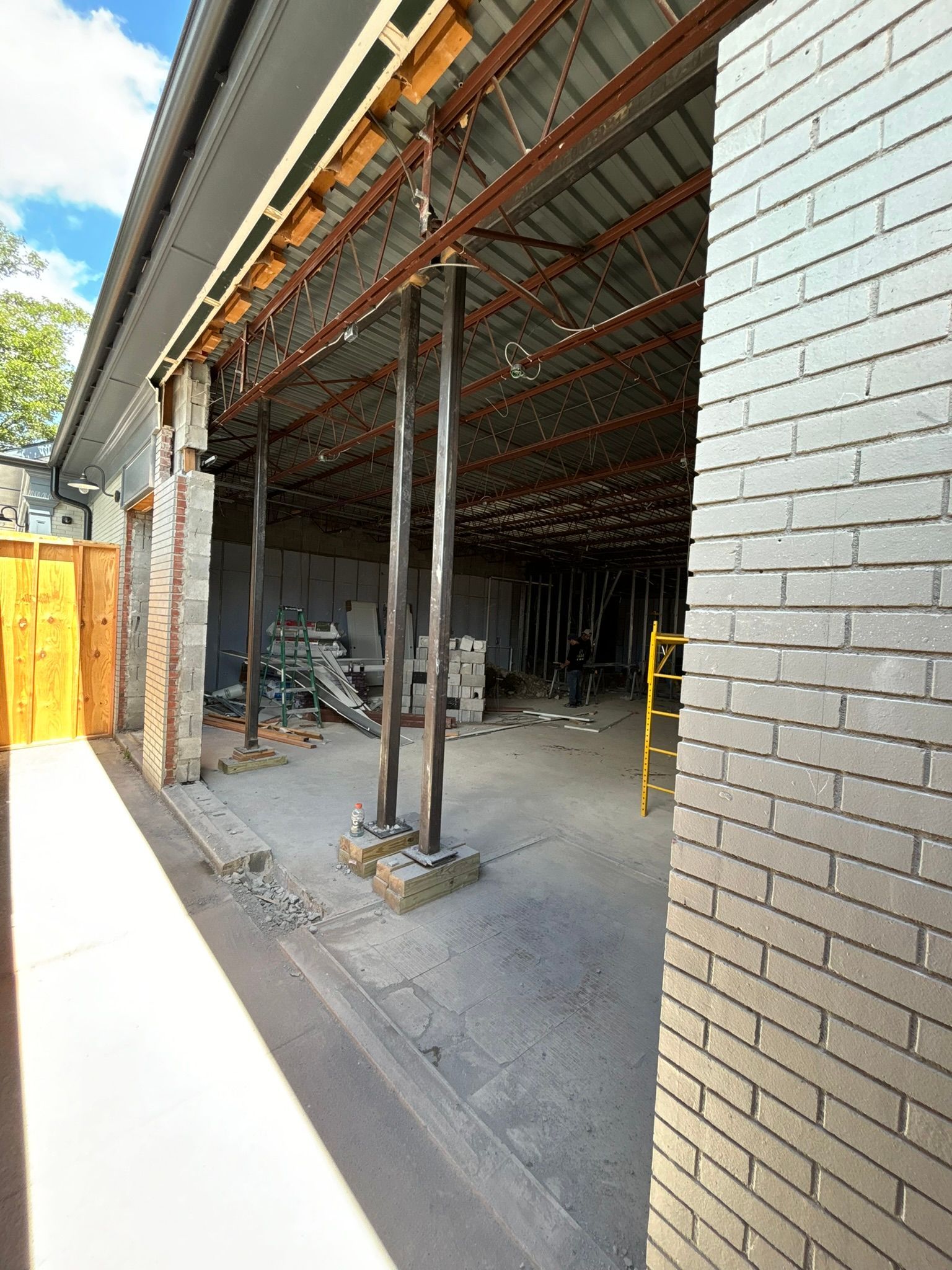 Construction site with exposed roof beams and brick walls. Steel support columns hold the roof up.