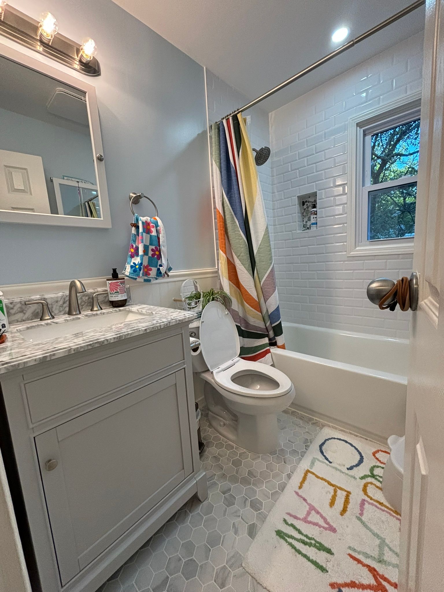 Bathroom with light blue walls, white vanity, patterned shower curtain, and hexagon tile floor.