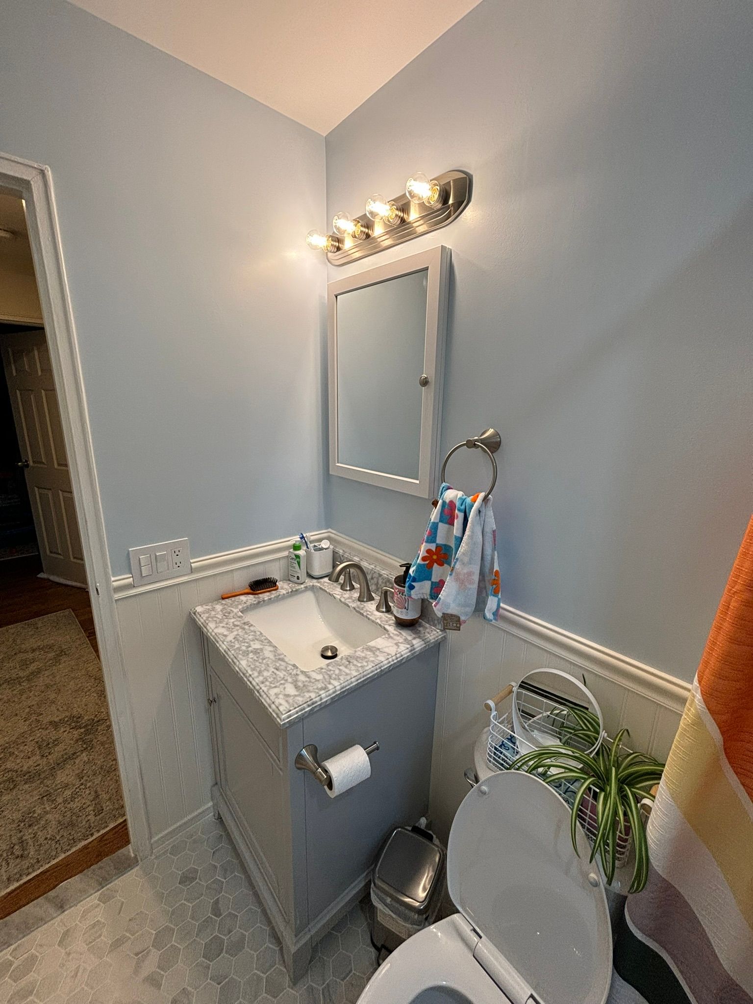 Small bathroom with gray vanity, toilet, mirror, towel, and light fixture; light blue walls.