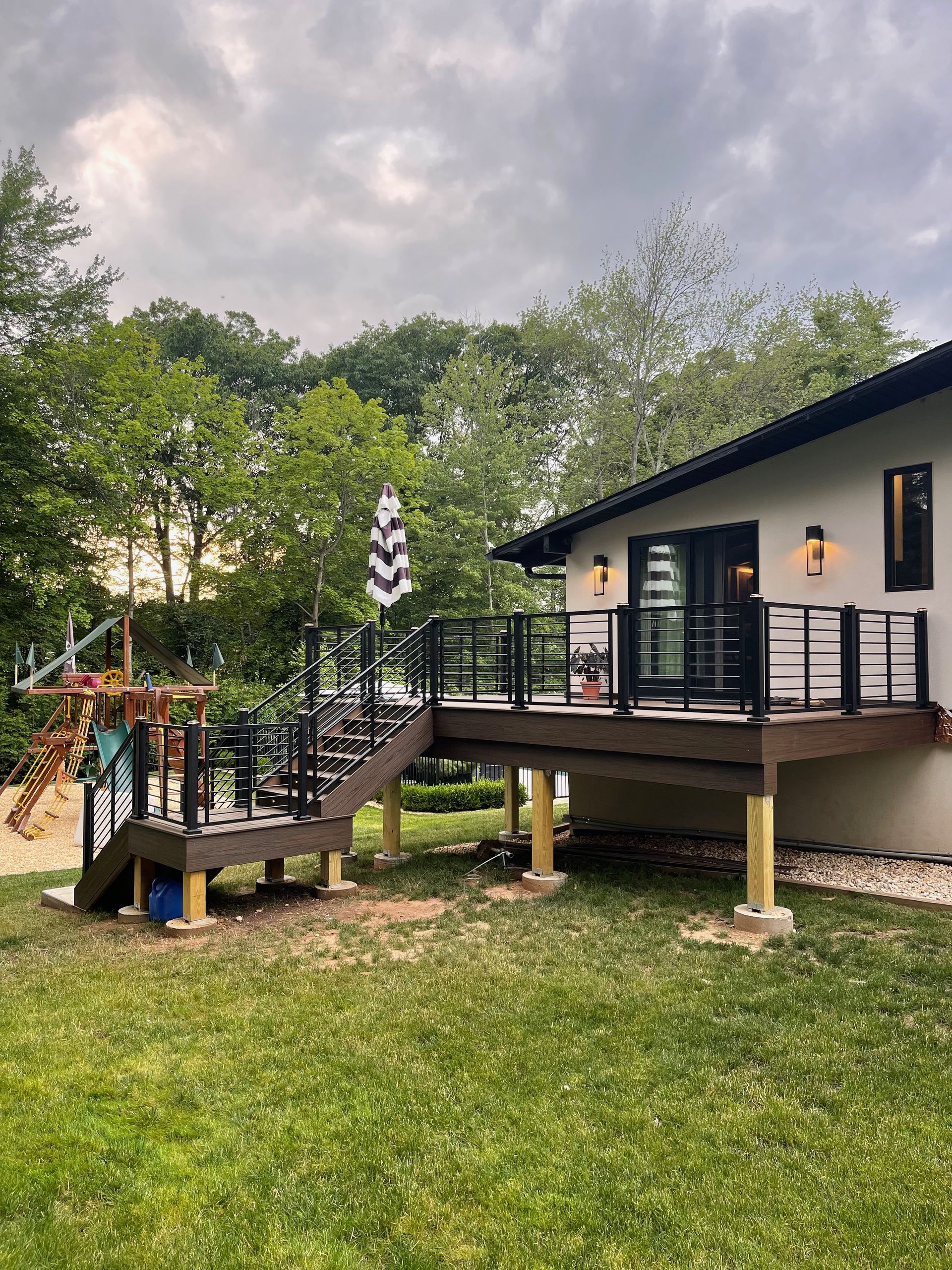 Backyard deck with black railings, a black and white umbrella, and a play set.