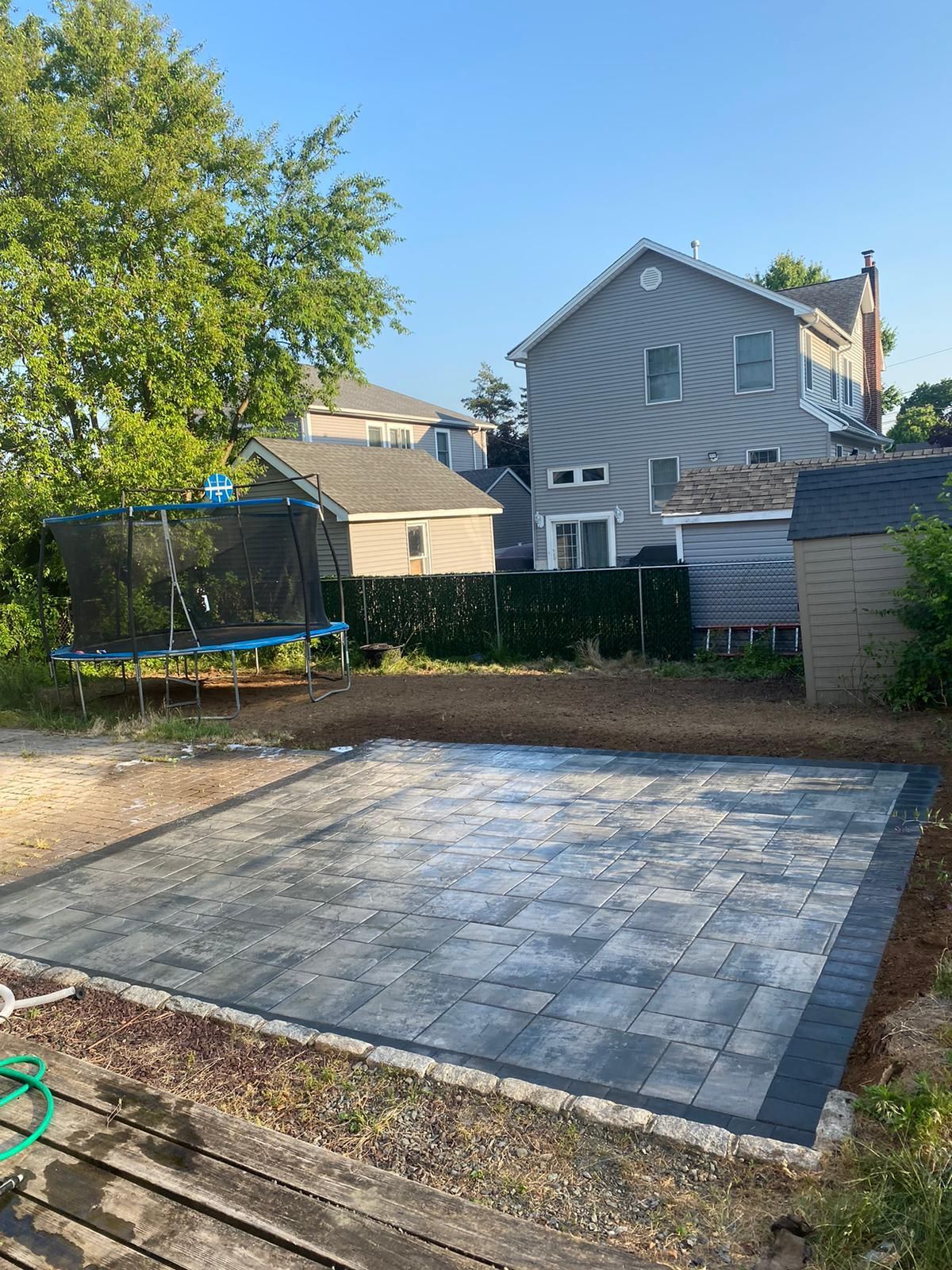 Backyard with a gray paver patio, trampoline, and houses in the background.