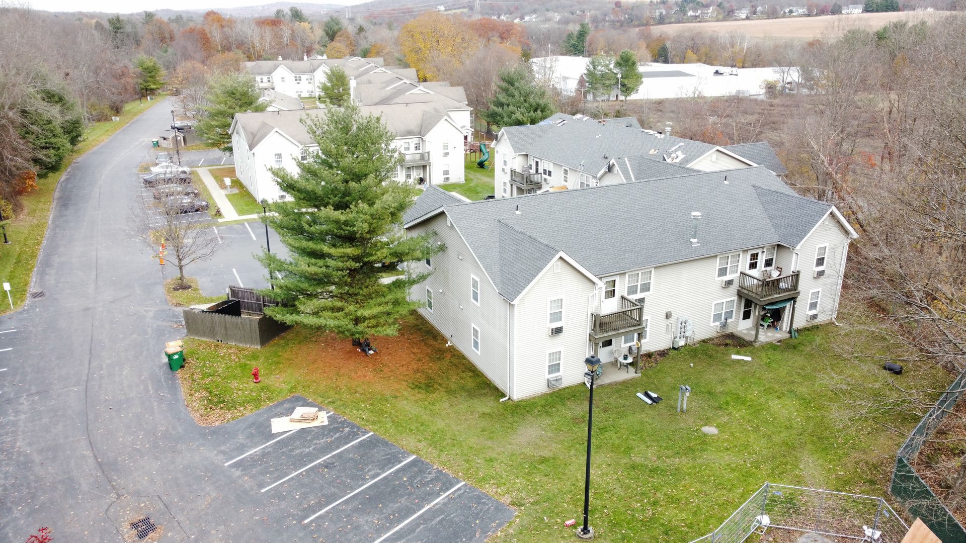 Aerial view of apartment buildings with parking, trees, and a road on an overcast day.