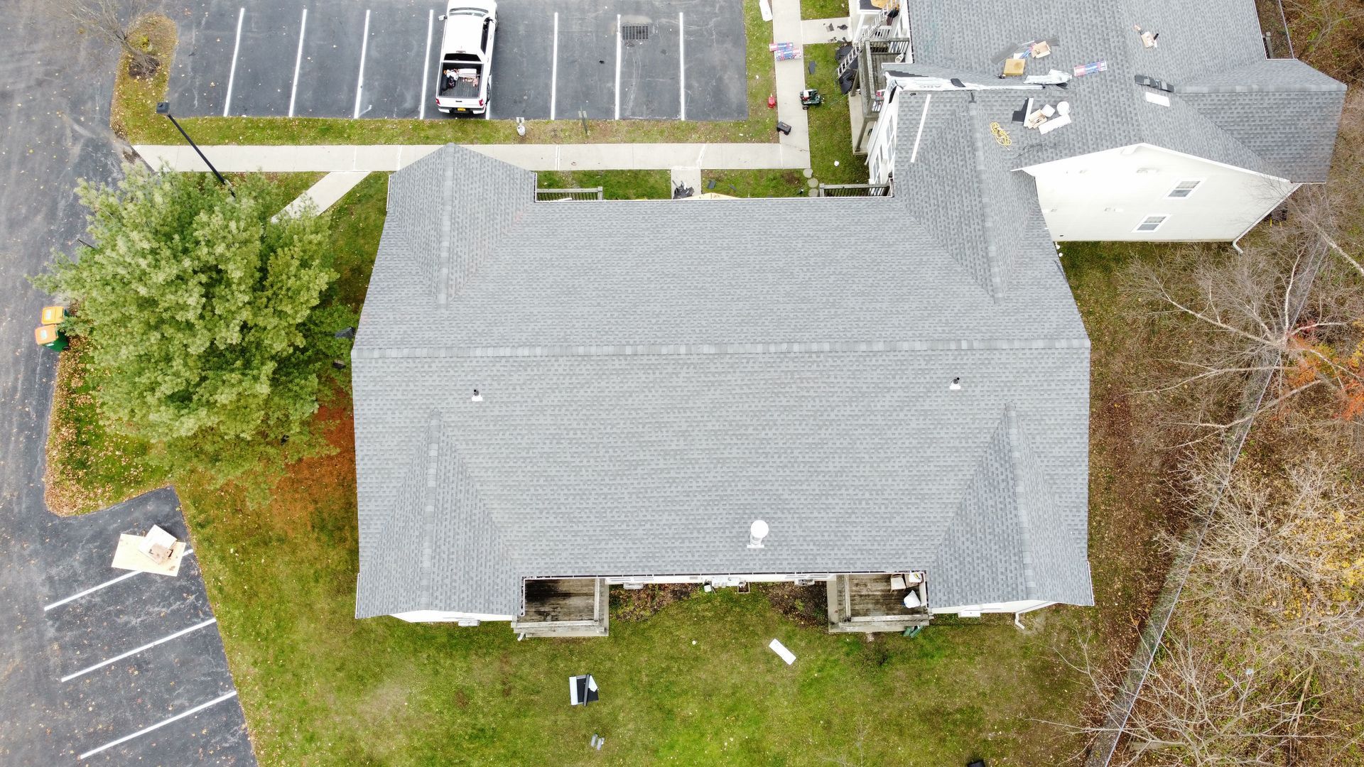Aerial view of a grey-roofed building with a parking lot and trees nearby.
