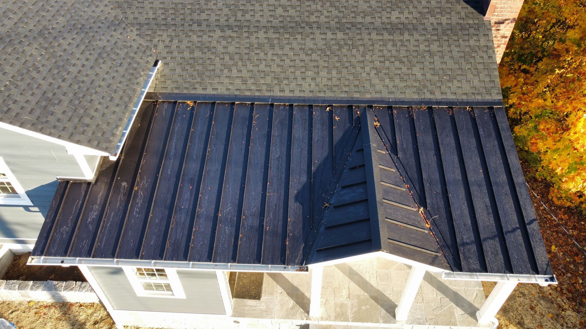 Overhead view of a house with a gray roof and black metal roof. Fall foliage surrounds the building.