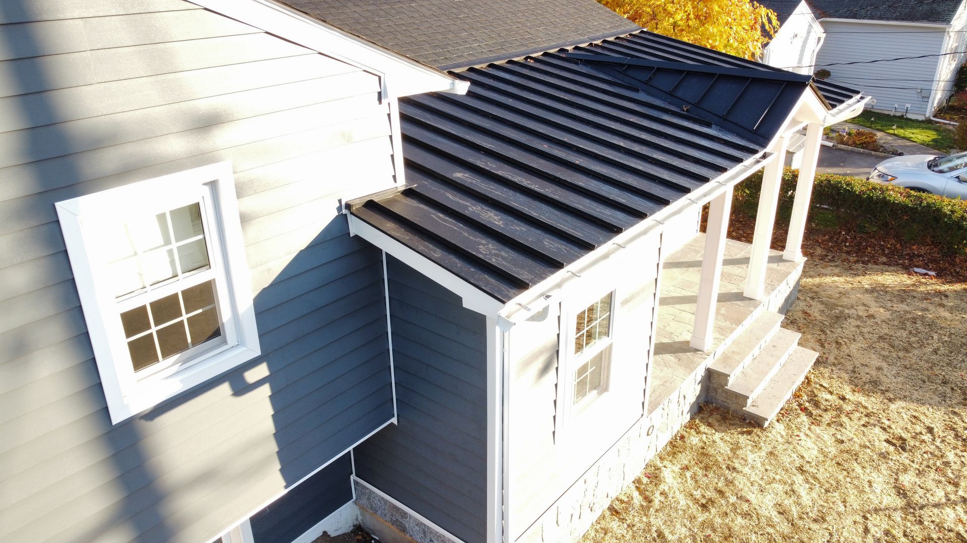Blue house with a black metal roof and white trim. Porch with columns, two windows.