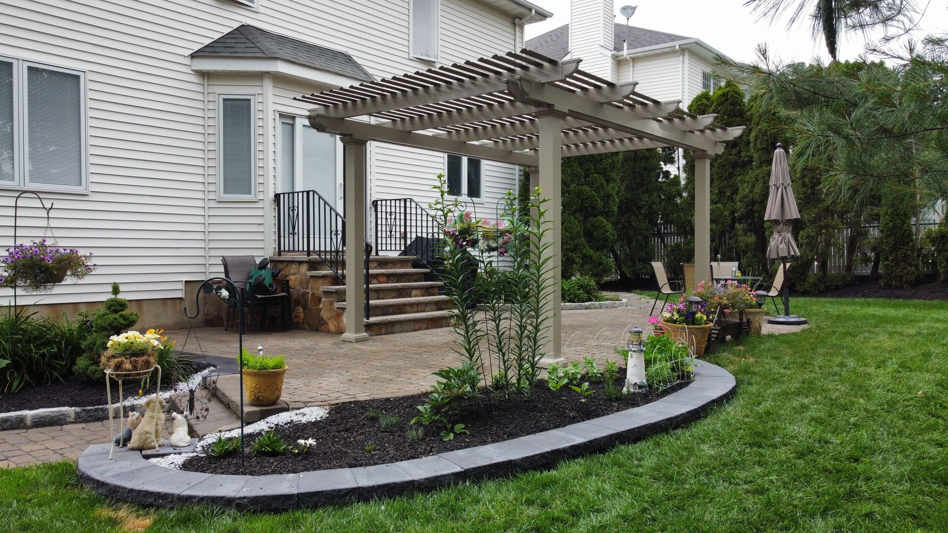 Backyard patio with pergola, landscaping, and steps leading to a house.