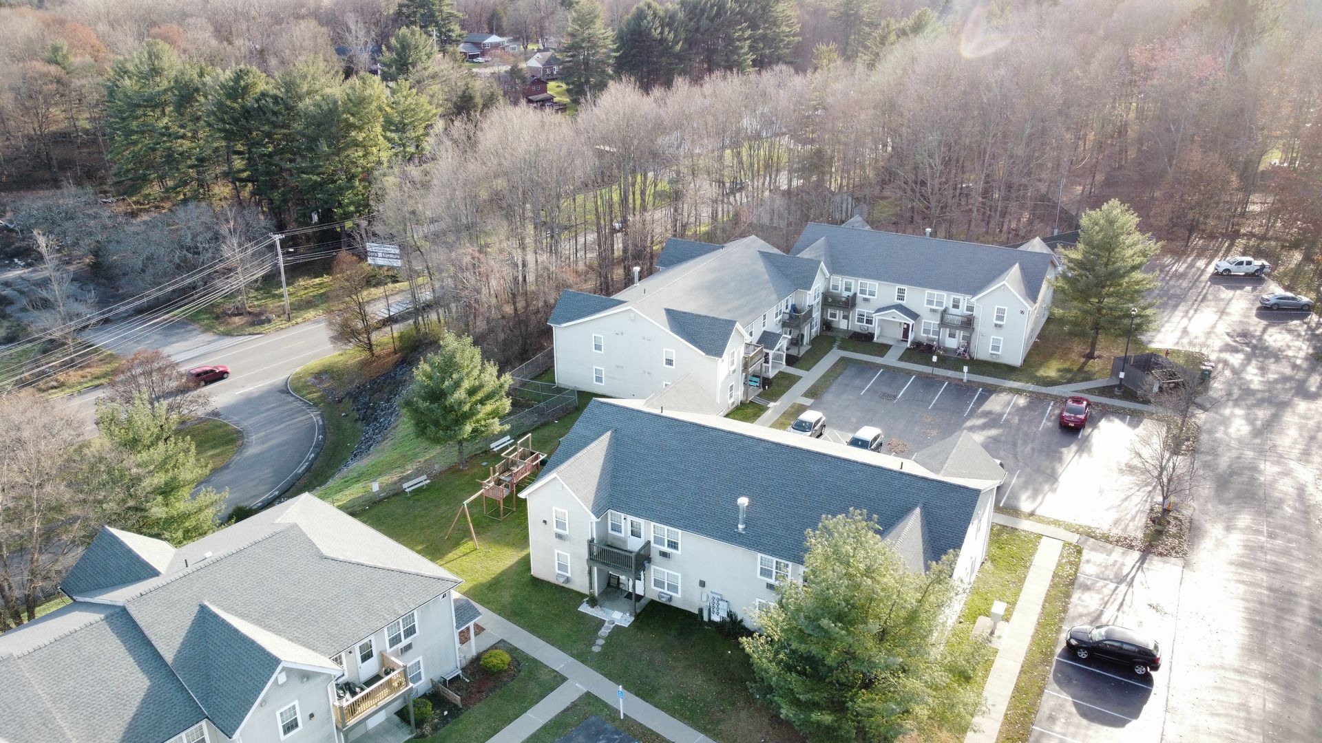 Aerial view of beige apartment buildings, parking lot, and trees on a cloudy day.