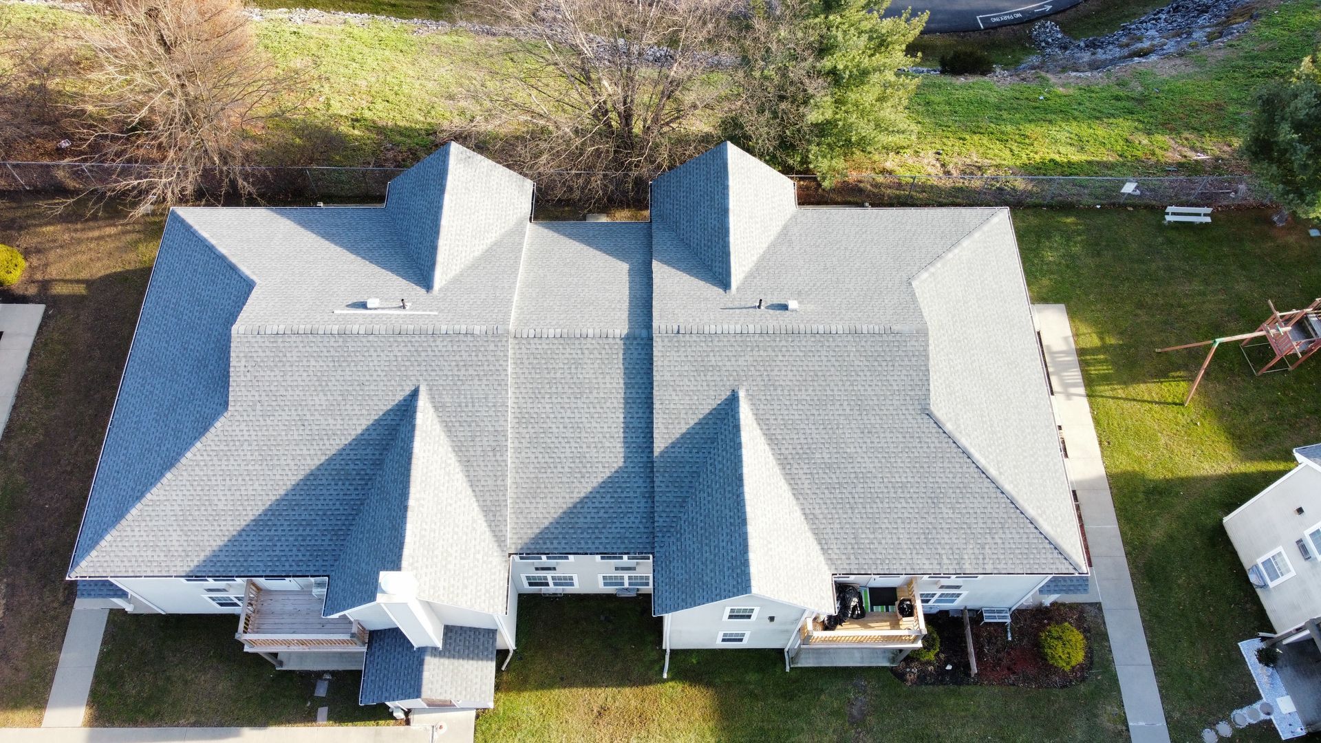 Overhead view of a pair of gray-roofed connected townhouses surrounded by green grass and trees.