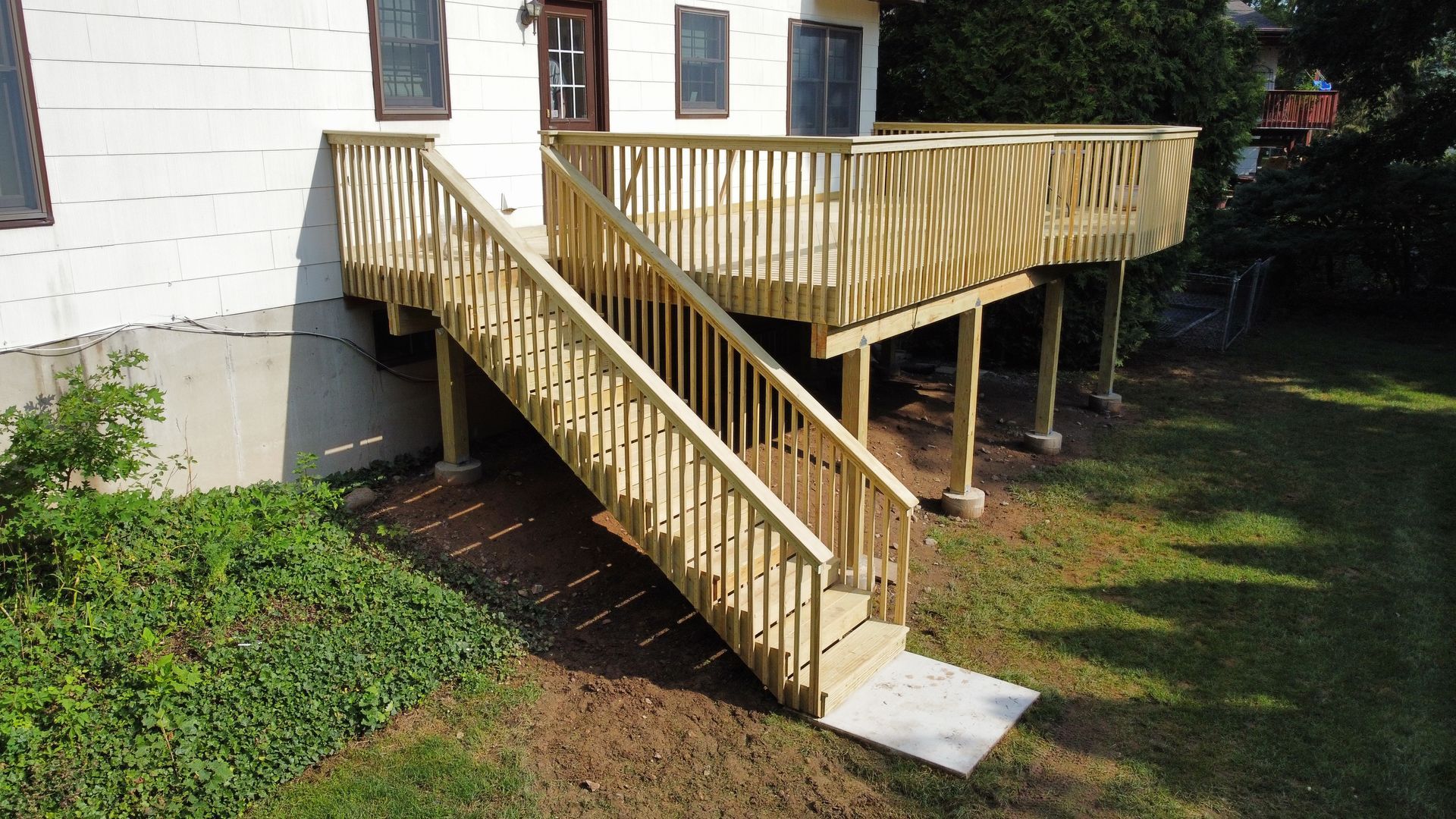 Wooden deck with stairs leading to a house entrance, set in a grassy yard.