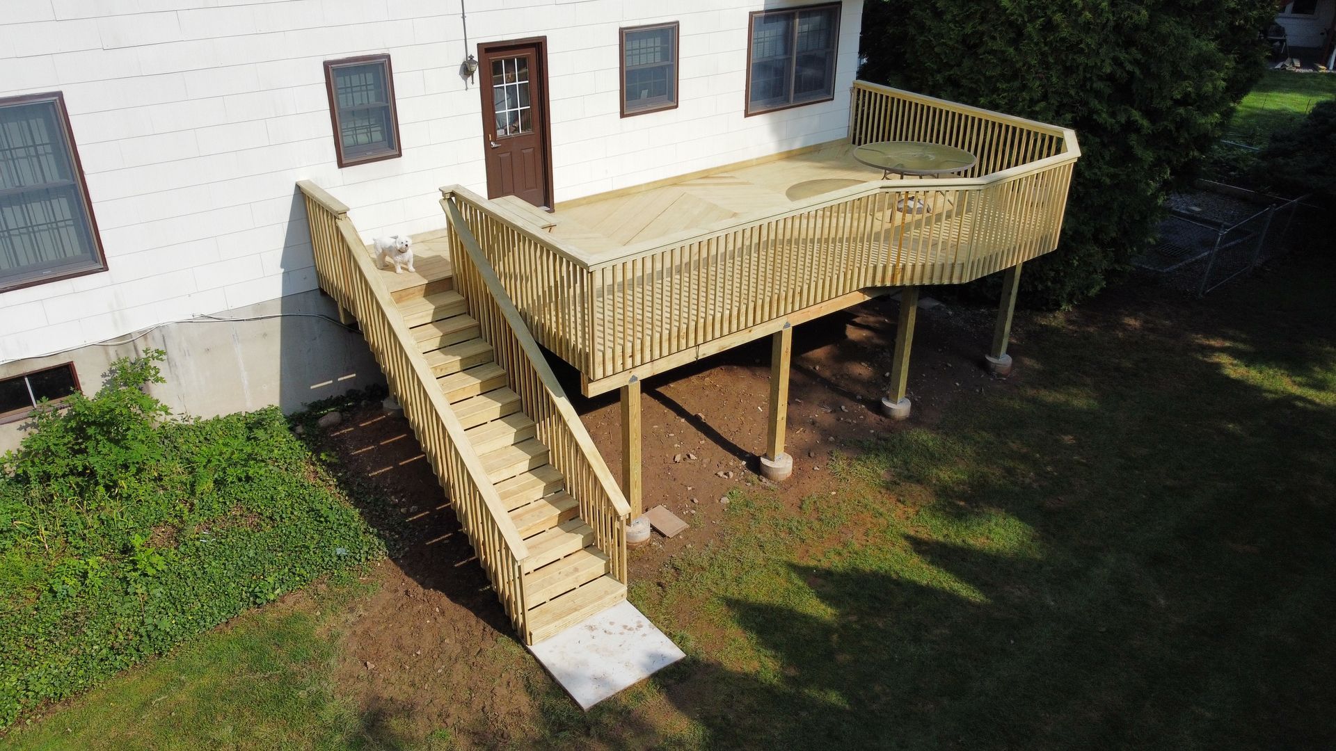 Wooden deck with stairs leading from a white house to a grassy yard.
