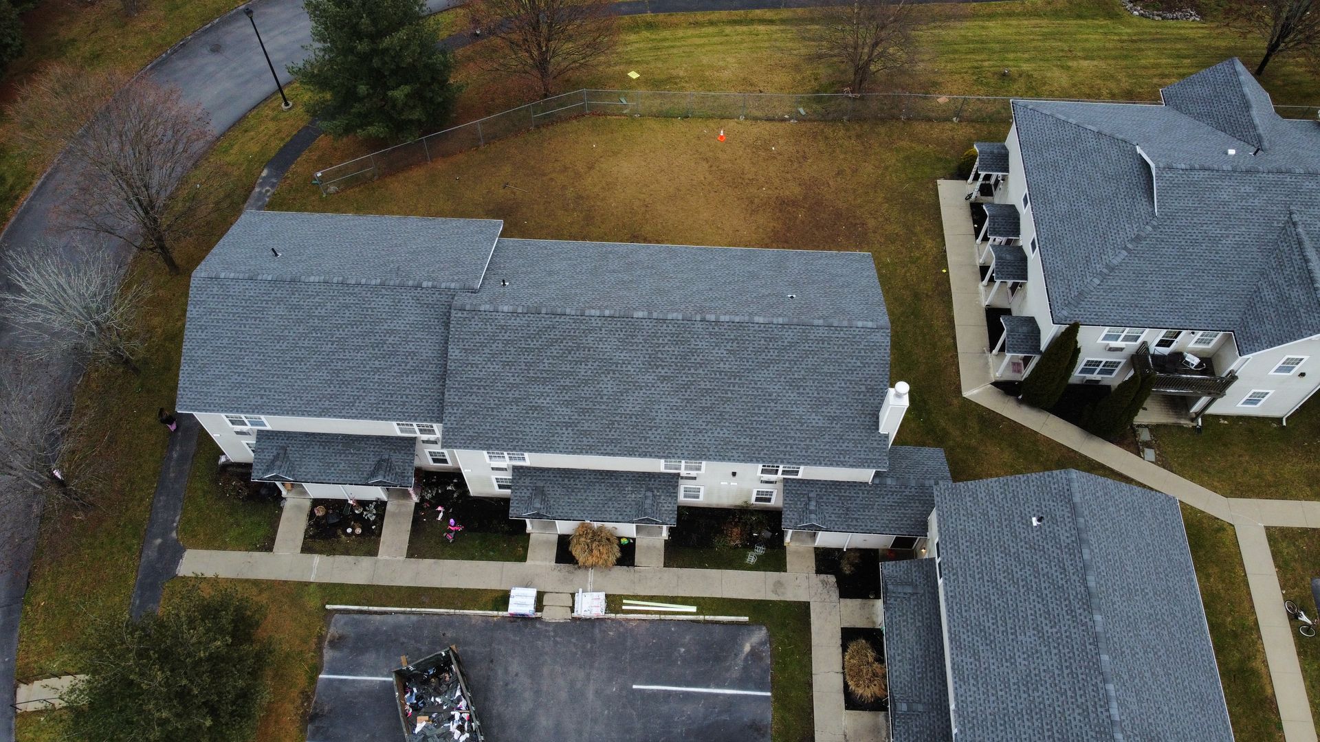 Aerial view of gray-roofed townhouses with small front yards and a curved road in a residential area.