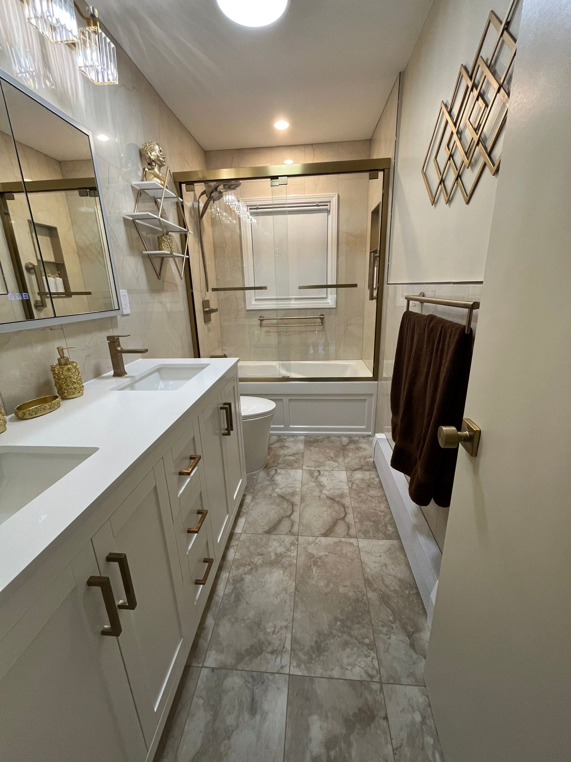 Bathroom with white vanity, gold fixtures, beige tile, and a shower with a gold-framed glass door.