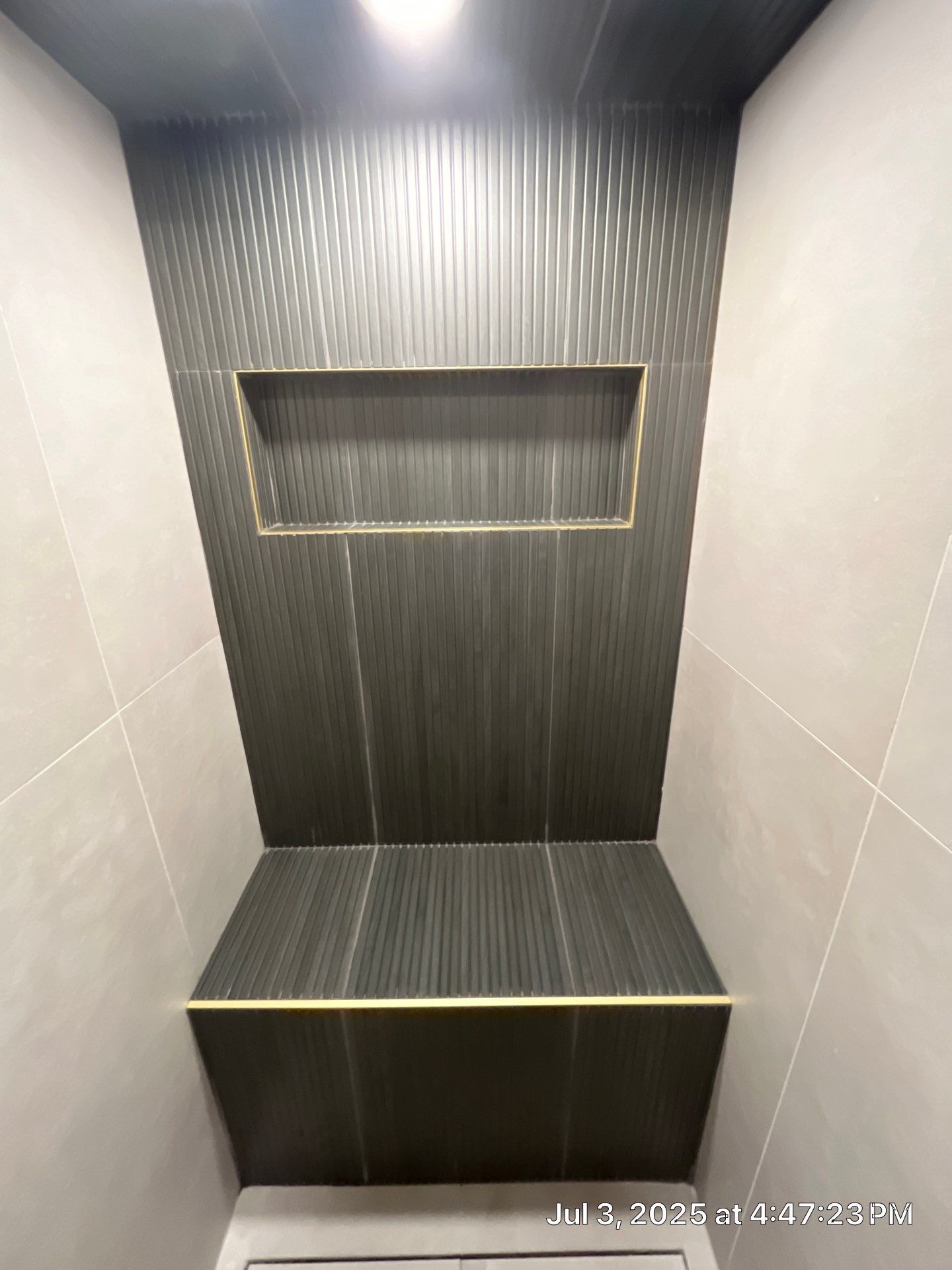 Dark gray tiled shower niche with gold trim and built-in bench.