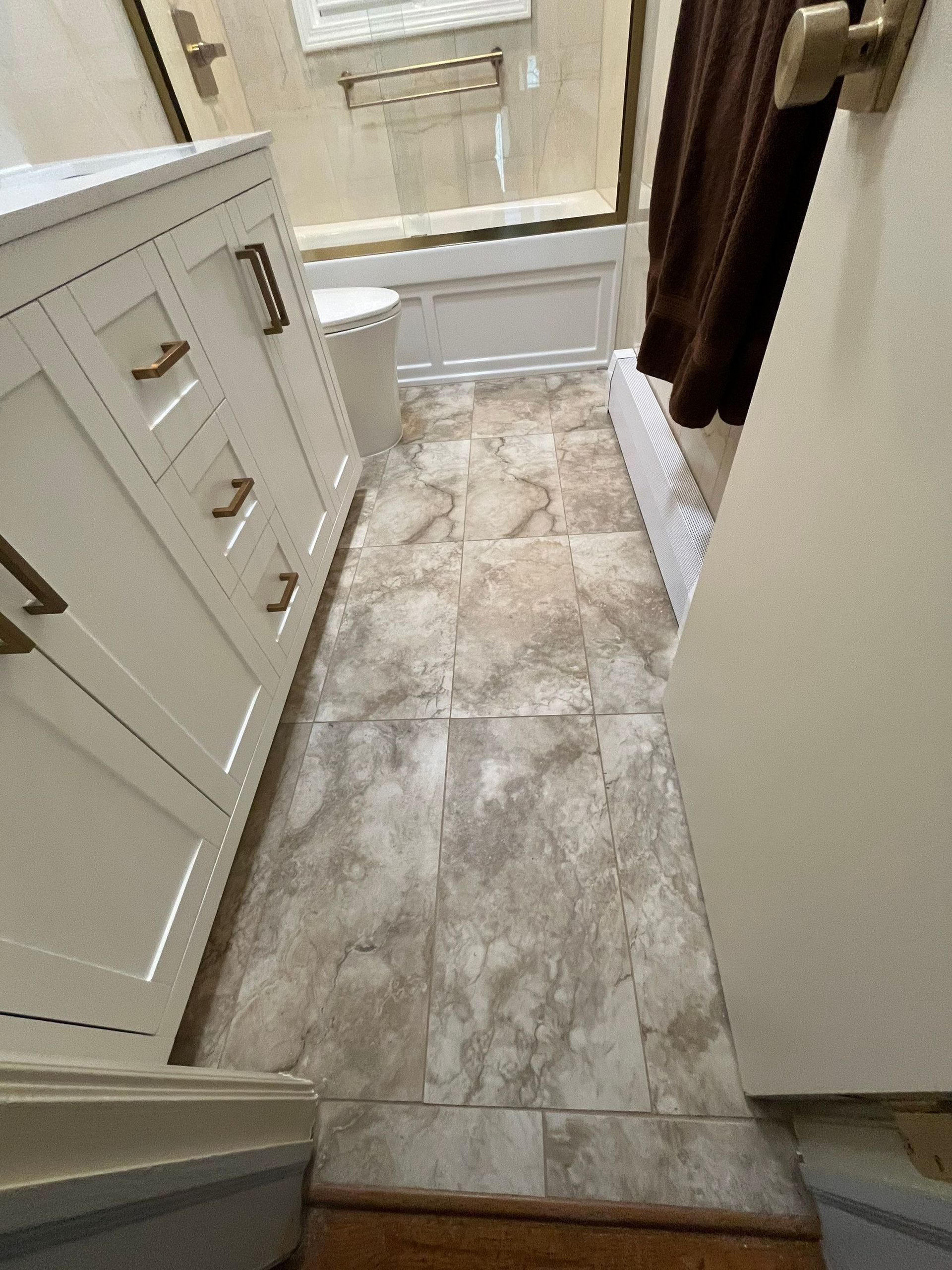 Bathroom with beige tile floor, white vanity with bronze handles, and brown shower curtain.