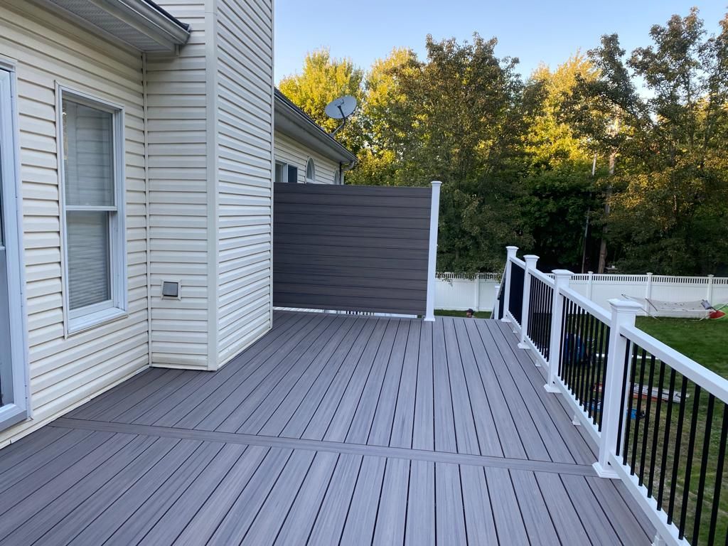 Gray composite deck with white railing, a privacy screen, and a house exterior.