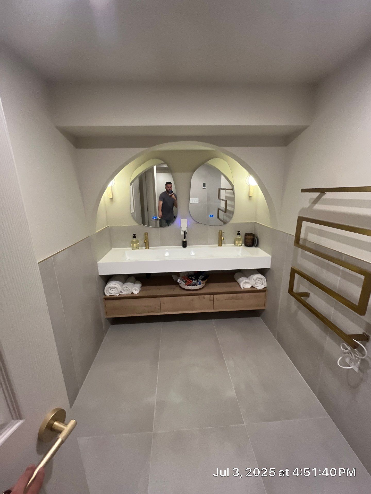 Modern bathroom with double sink, arched mirrors, and gold accents.