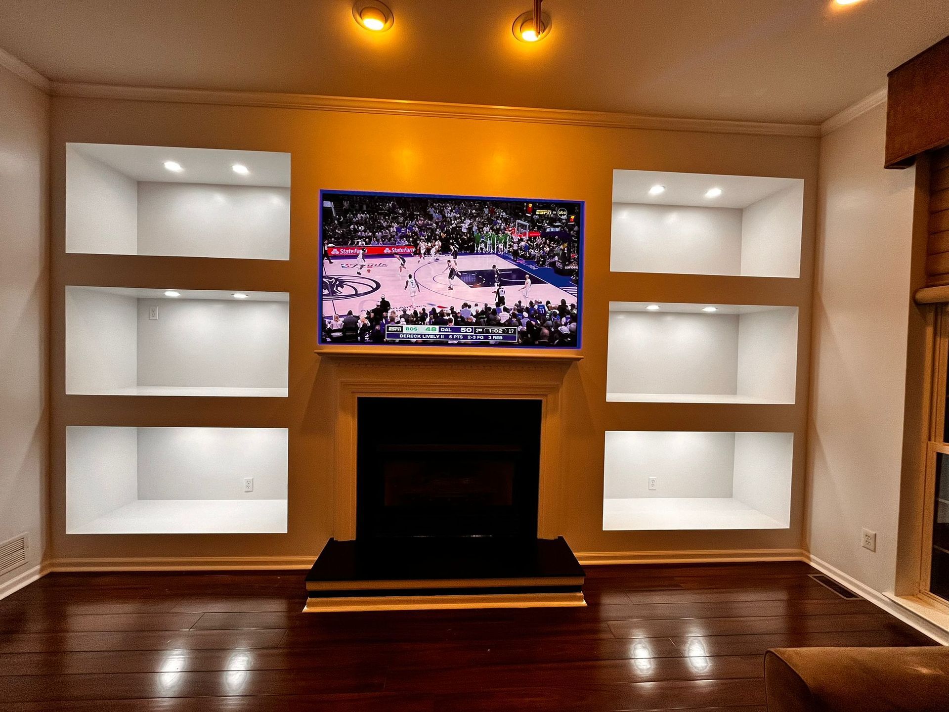 Living room with built-in white shelves around a TV and fireplace; dark wood floor.