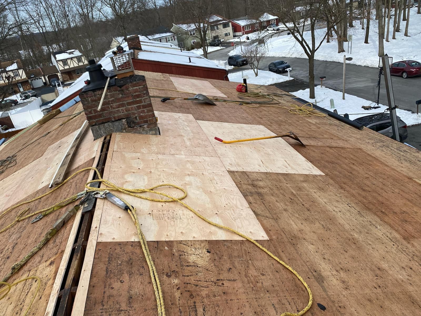 Rooftop repair: Workers replacing plywood. A yellow rope is for safety. Snowy residential area.