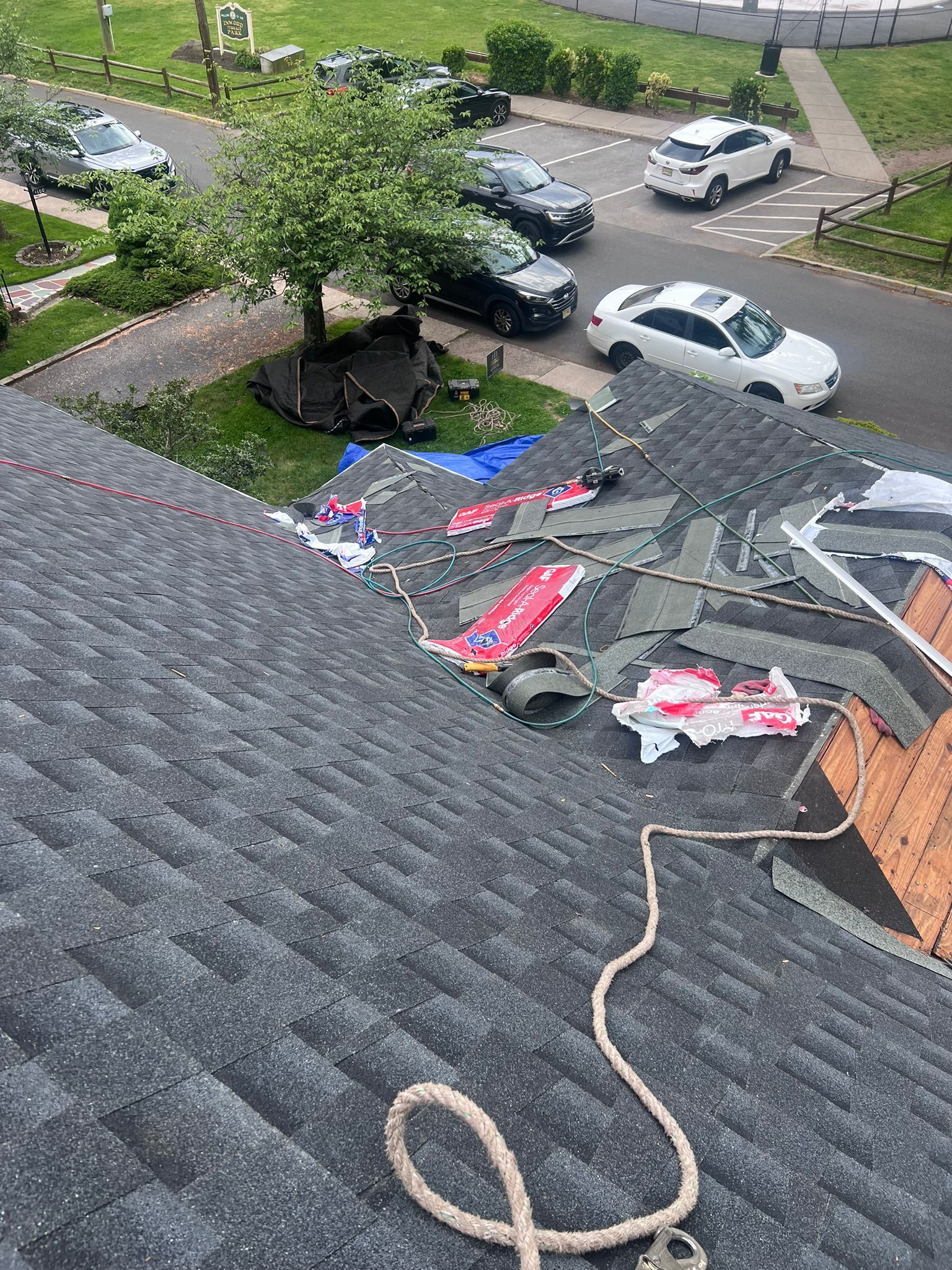 Damaged roof with missing shingles; rope tied to the edge. Cars and lawn in the background.